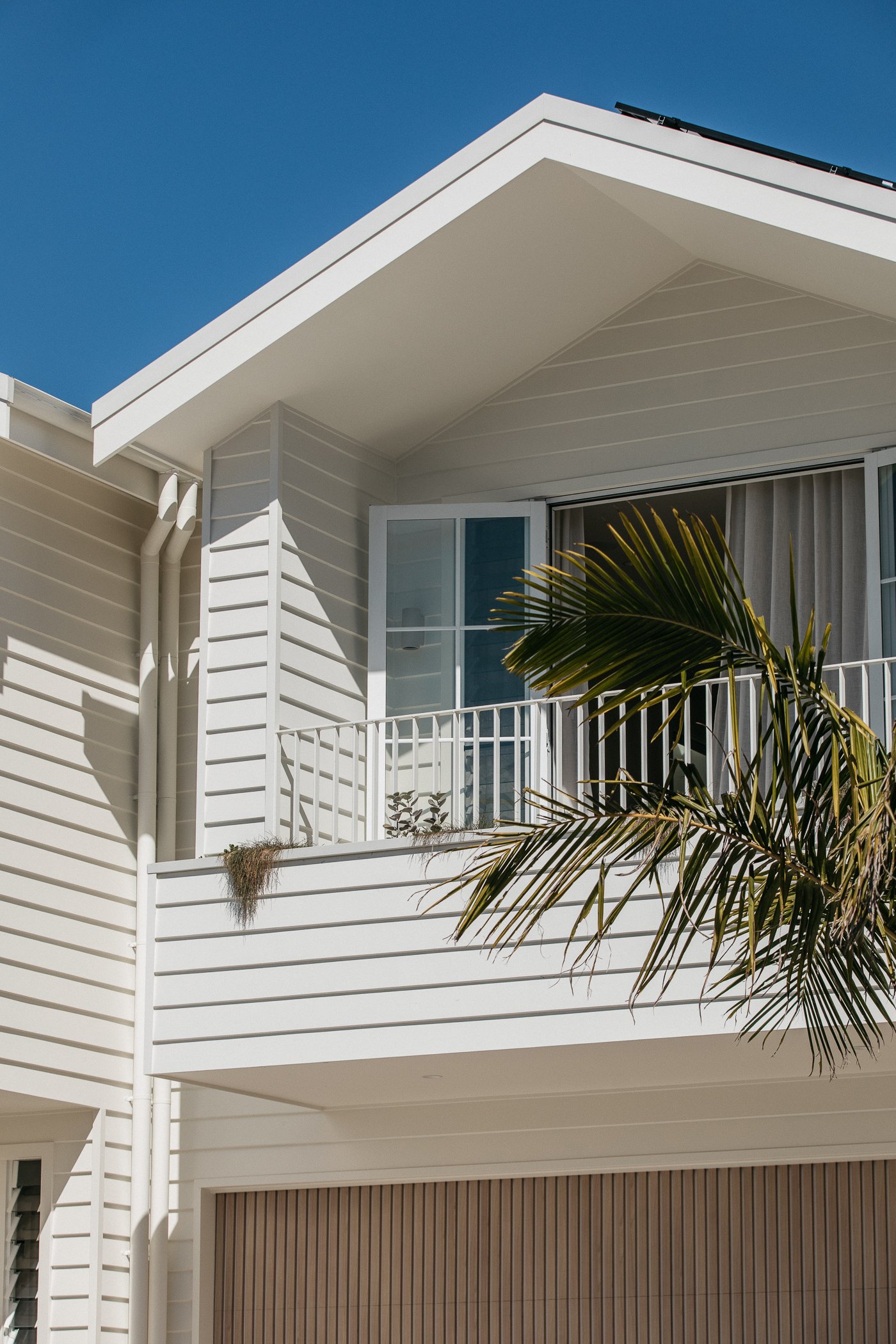 Modern white house with a balcony, large windows, and a palm tree, against a clear blue sky.