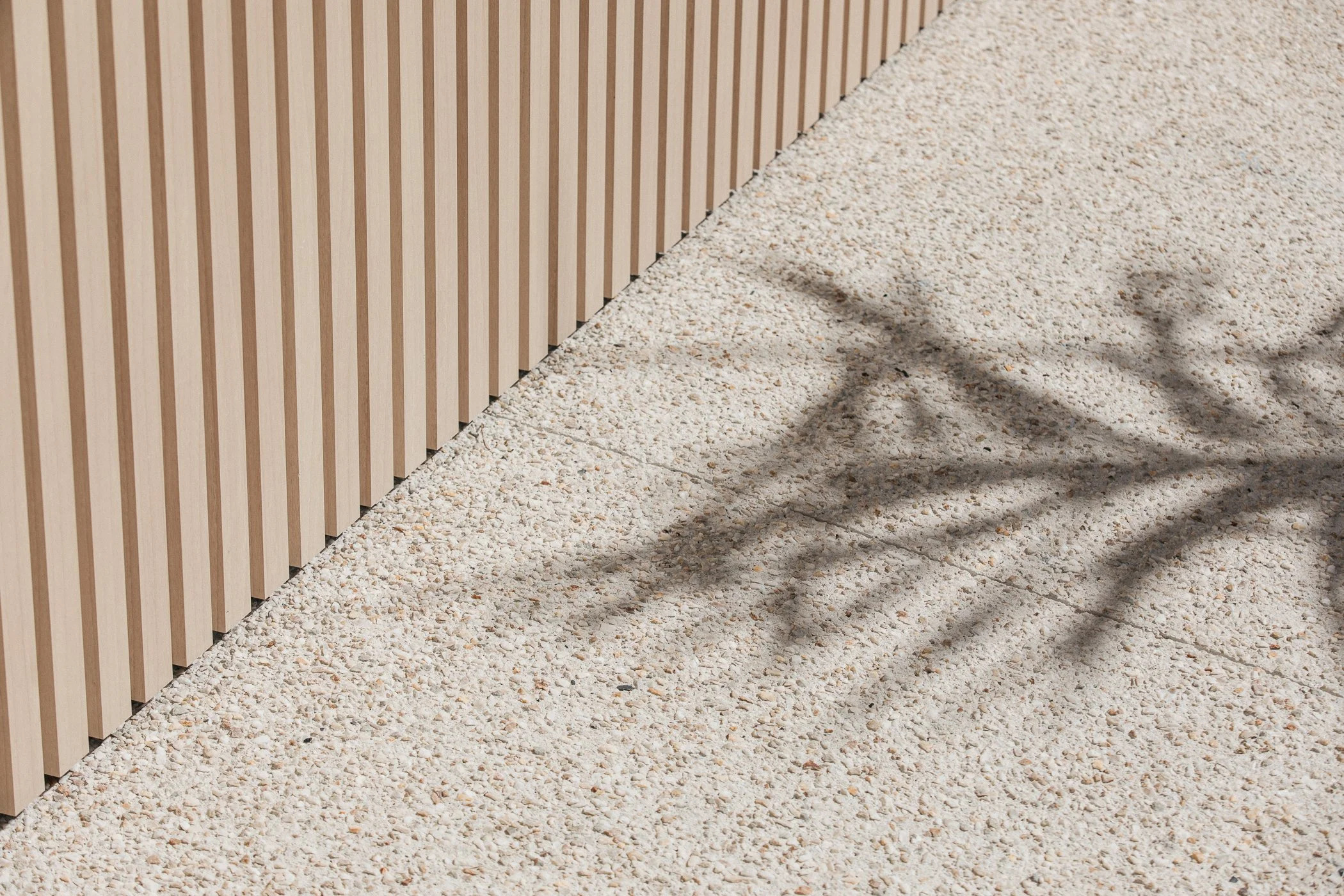 Close-up of a wooden slat fence casting shadows on a gravel ground.