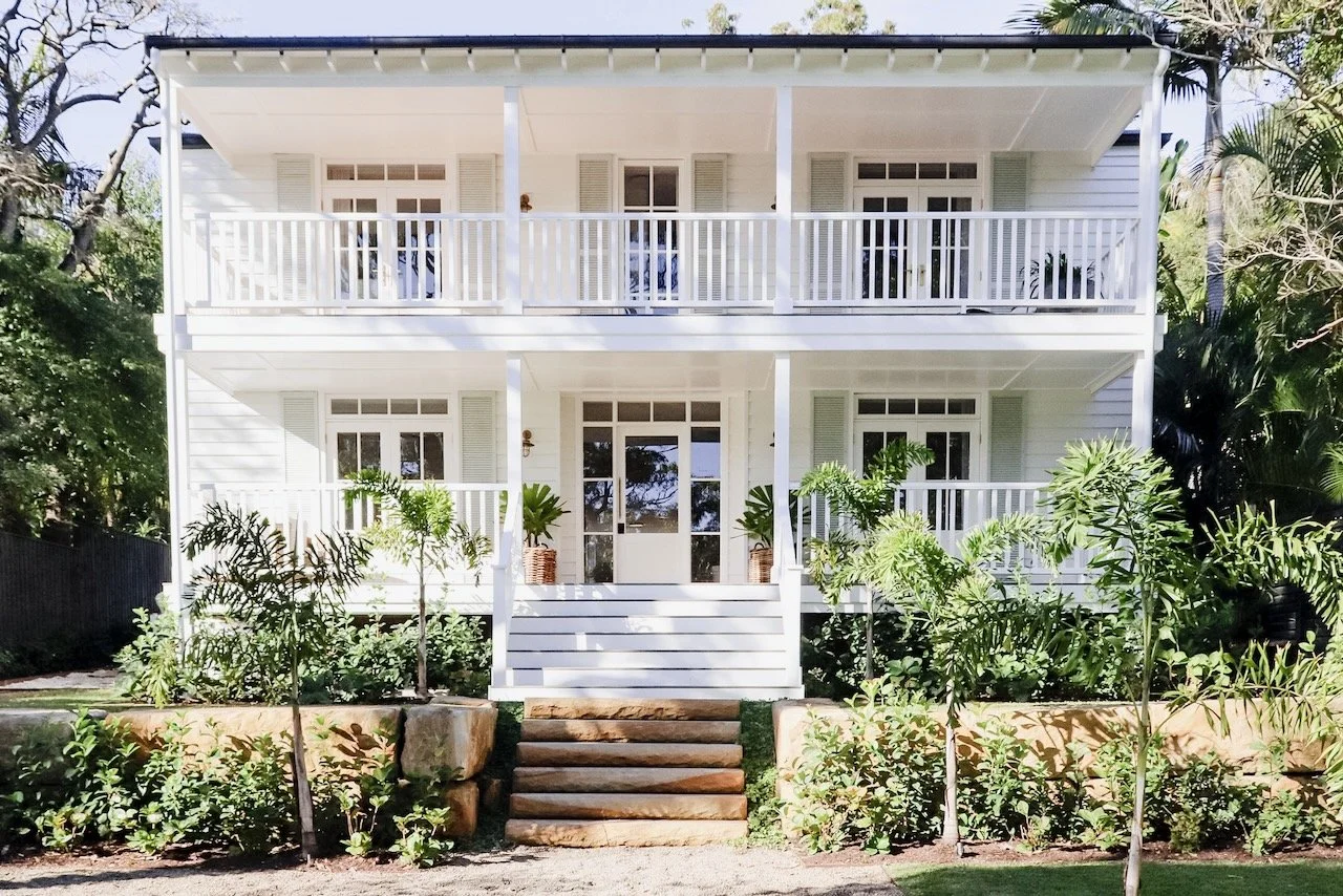 Two-story plantation style white house with a front porch and a balcony, surrounded by lush greenery and tropical plants built by HALIDAY.