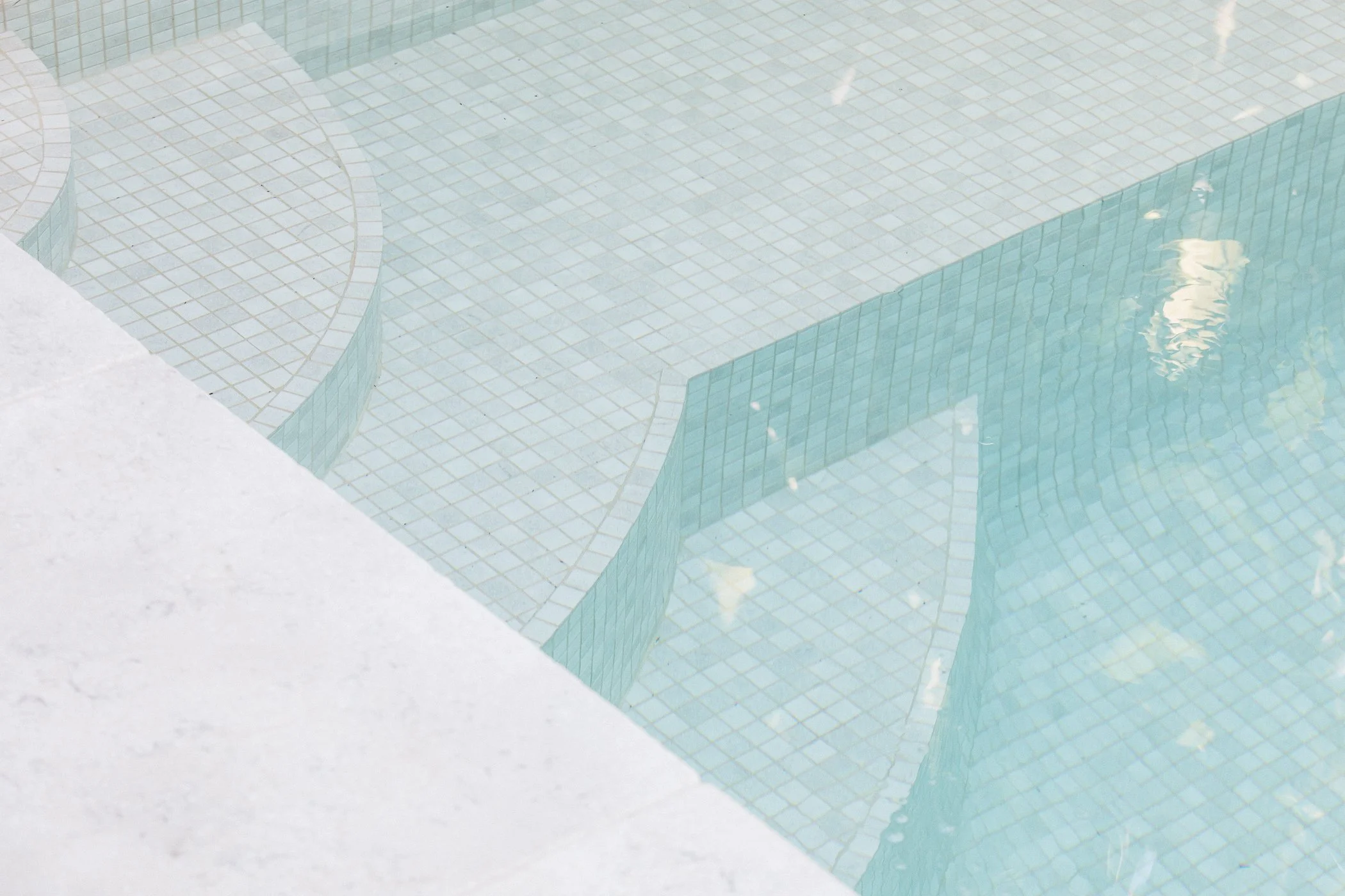 Empty swimming pool with tiled steps and shallow water, viewed from above.