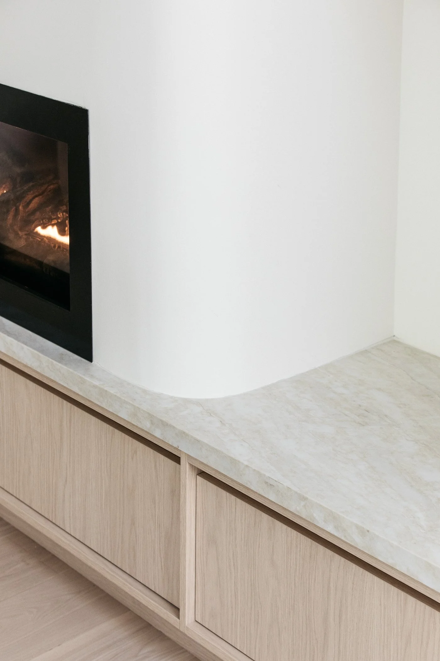 A modern fireplace set into a plain white wall, with a light-colored marble or granite countertop and wooden cabinetry below.