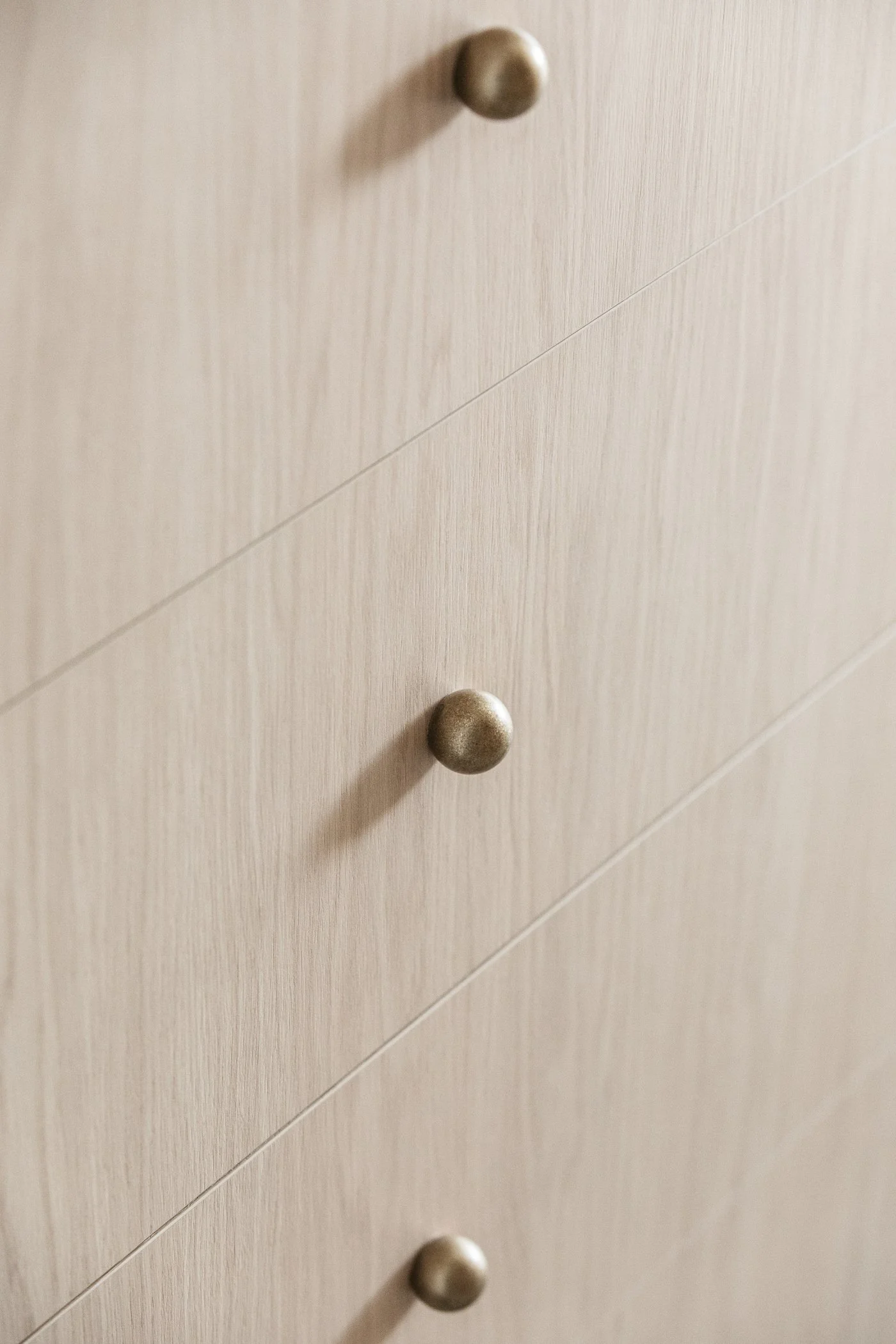 Close-up of a beige wooden dresser with horizontal panels and round metallic knobs.