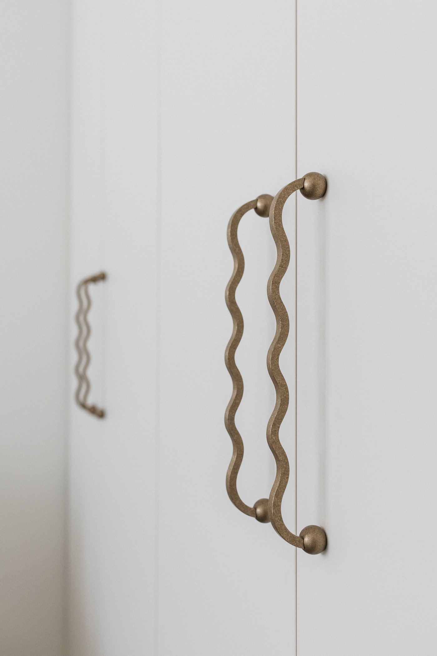 Close-up of a decorative wall hook with a wavy design, mounted on a white wall.