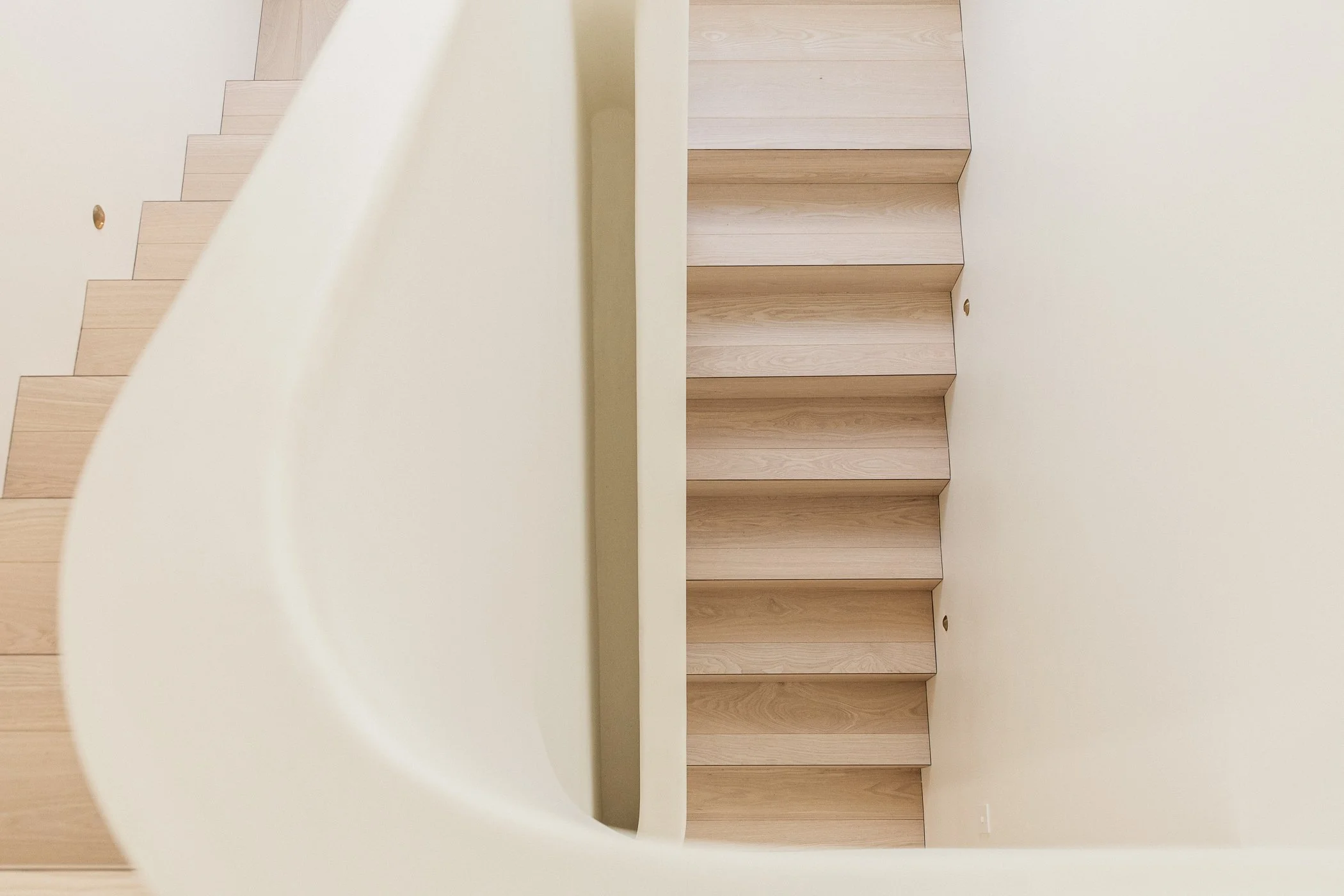 Curved staircase with natural oak ash timber detailing in a contemporary Casuarina home by HALIDAY.