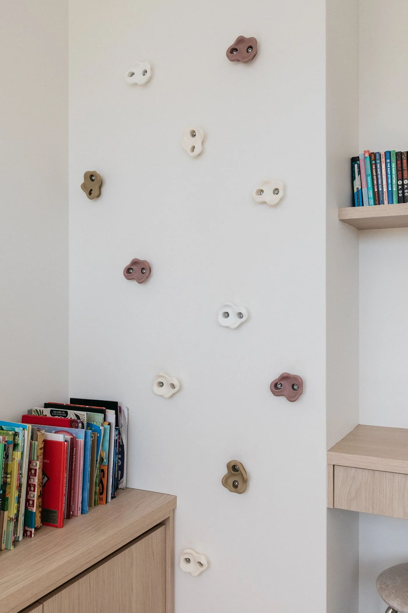 Indoor climbing wall with colorful handholds and a bookshelf filled with children's books.