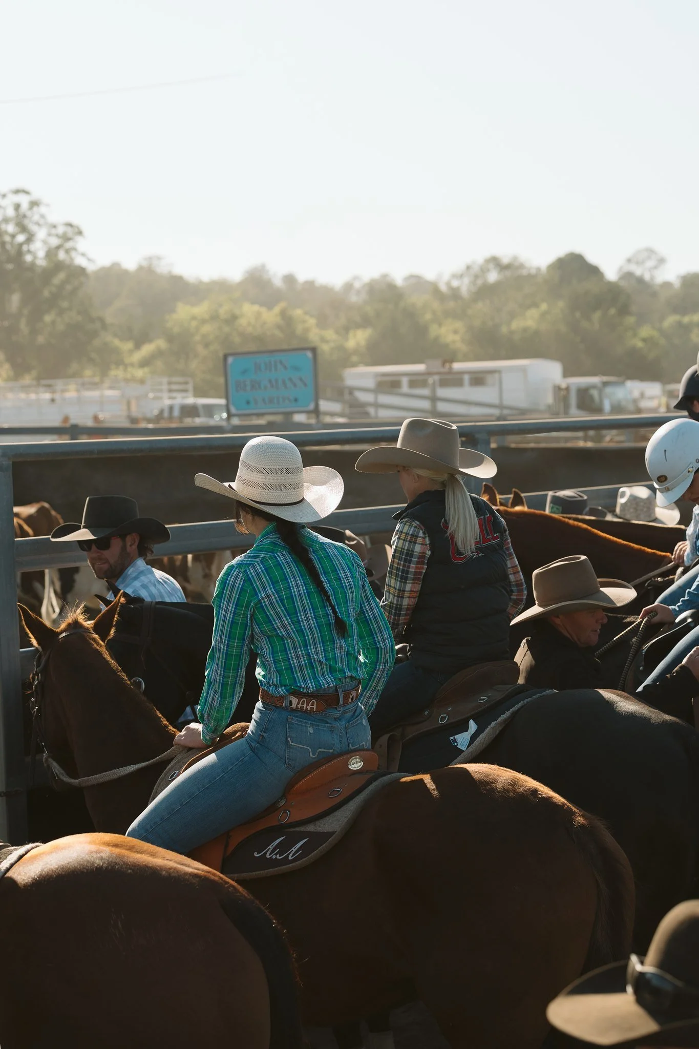 People riding horses at a rodeo event with a sign that reads "Join Beal Man" and trees in the background.
