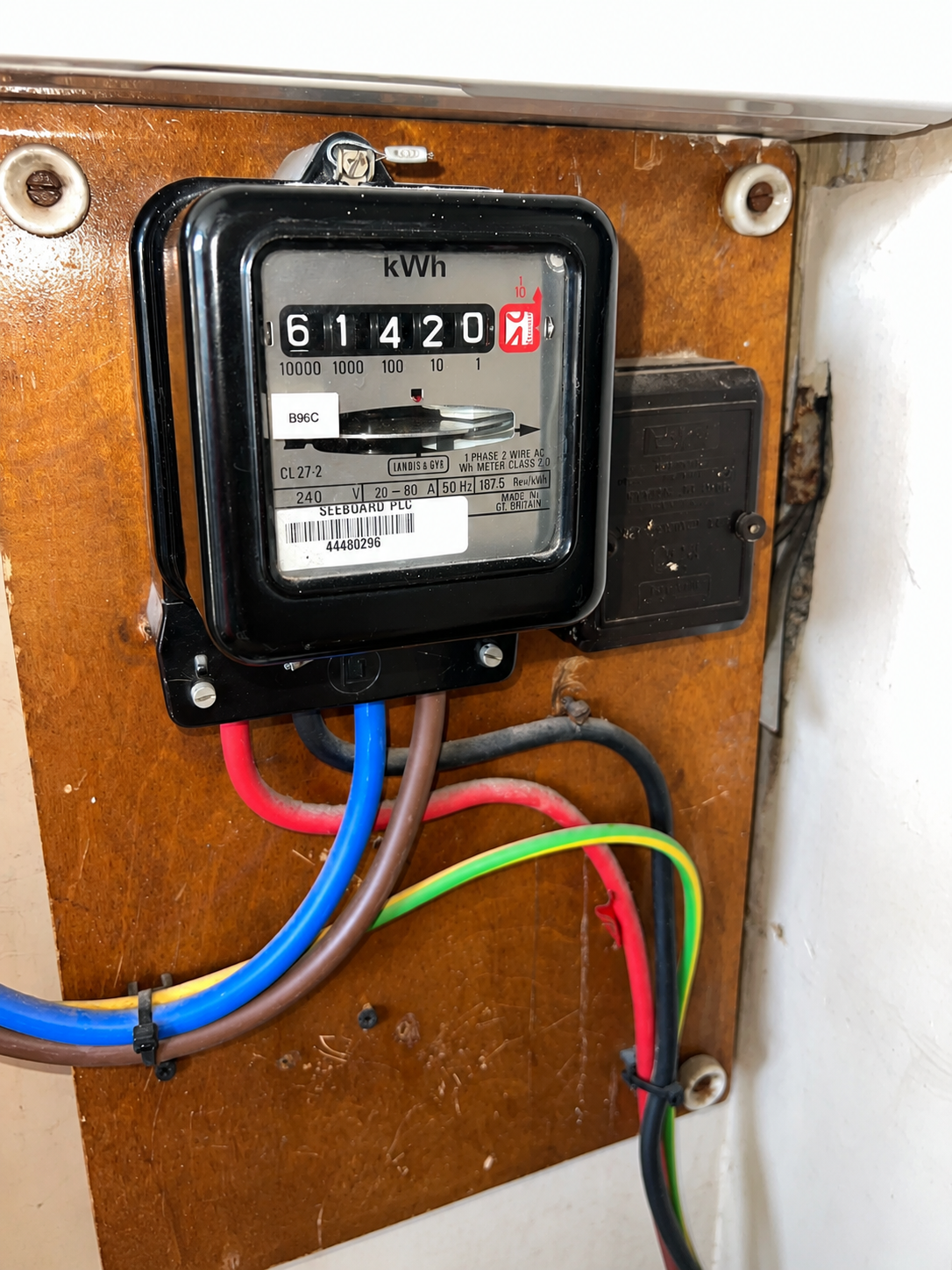 Electricity meter on a wooden panel with colored wires connected, used to measure electricity consumption.