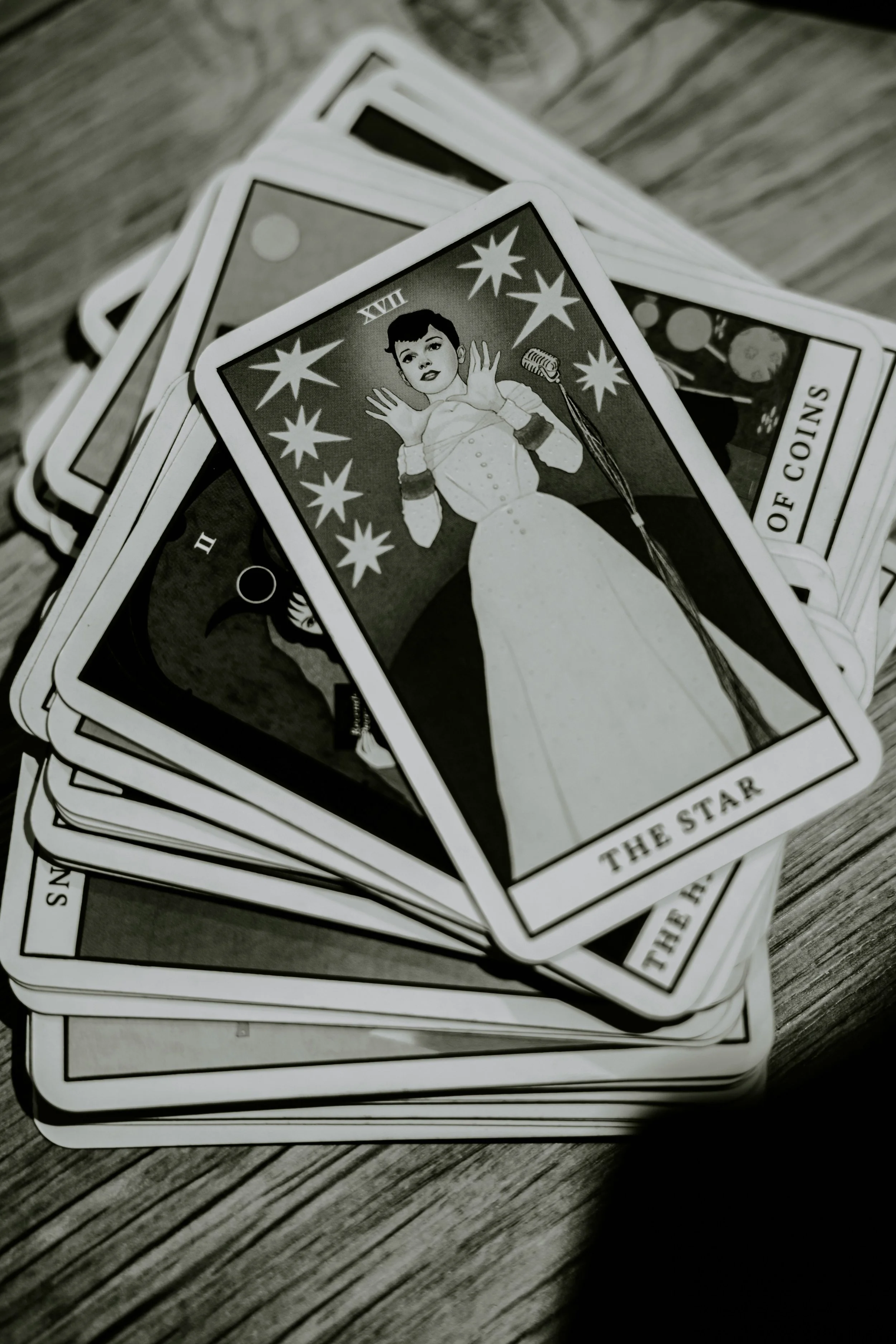 A pile of vintage-style tarot or oracle cards with black and white illustrations and text, laid on a wooden surface.