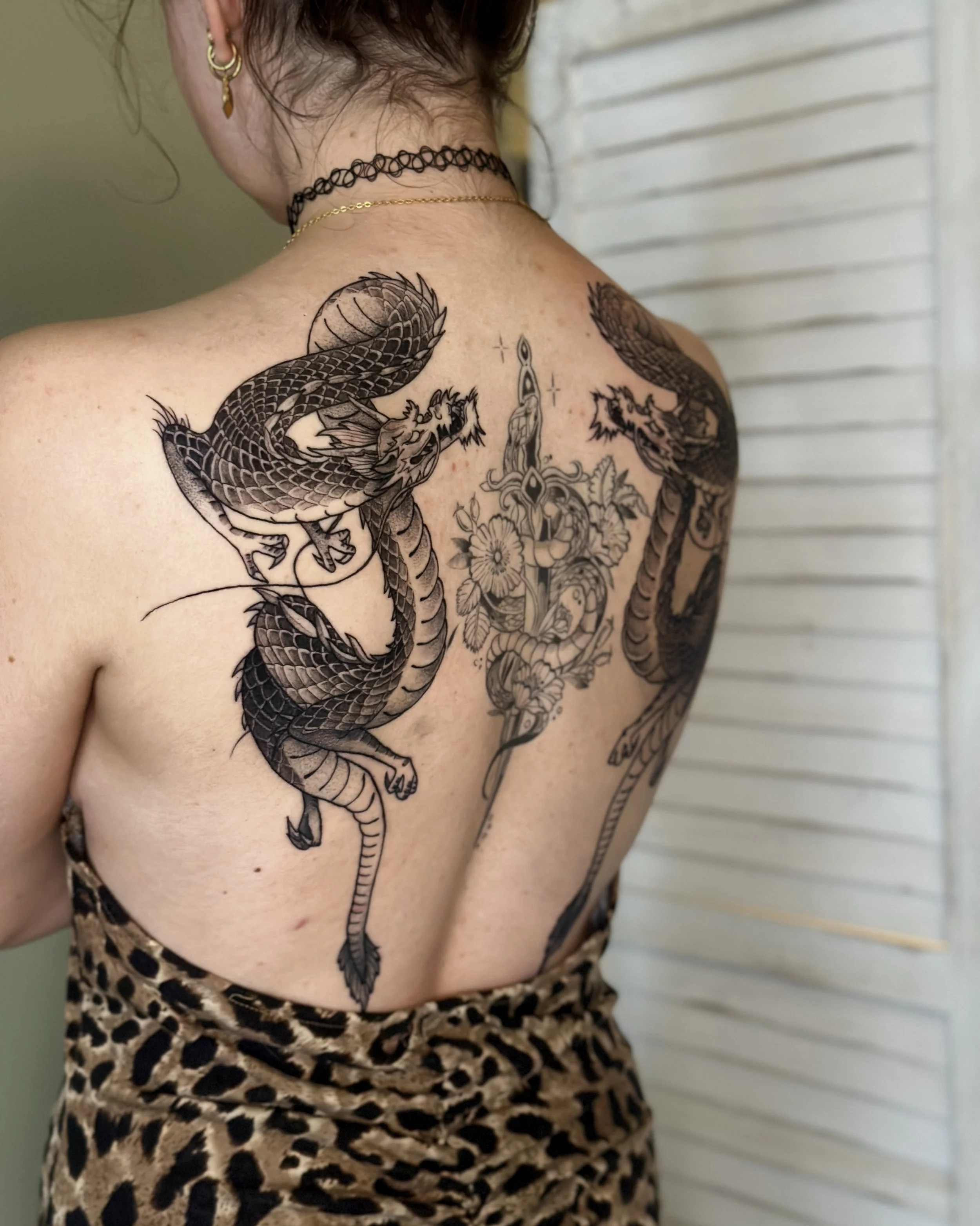 Close-up of a woman's back with a large, detailed tattoo of two symmetrical dragons.