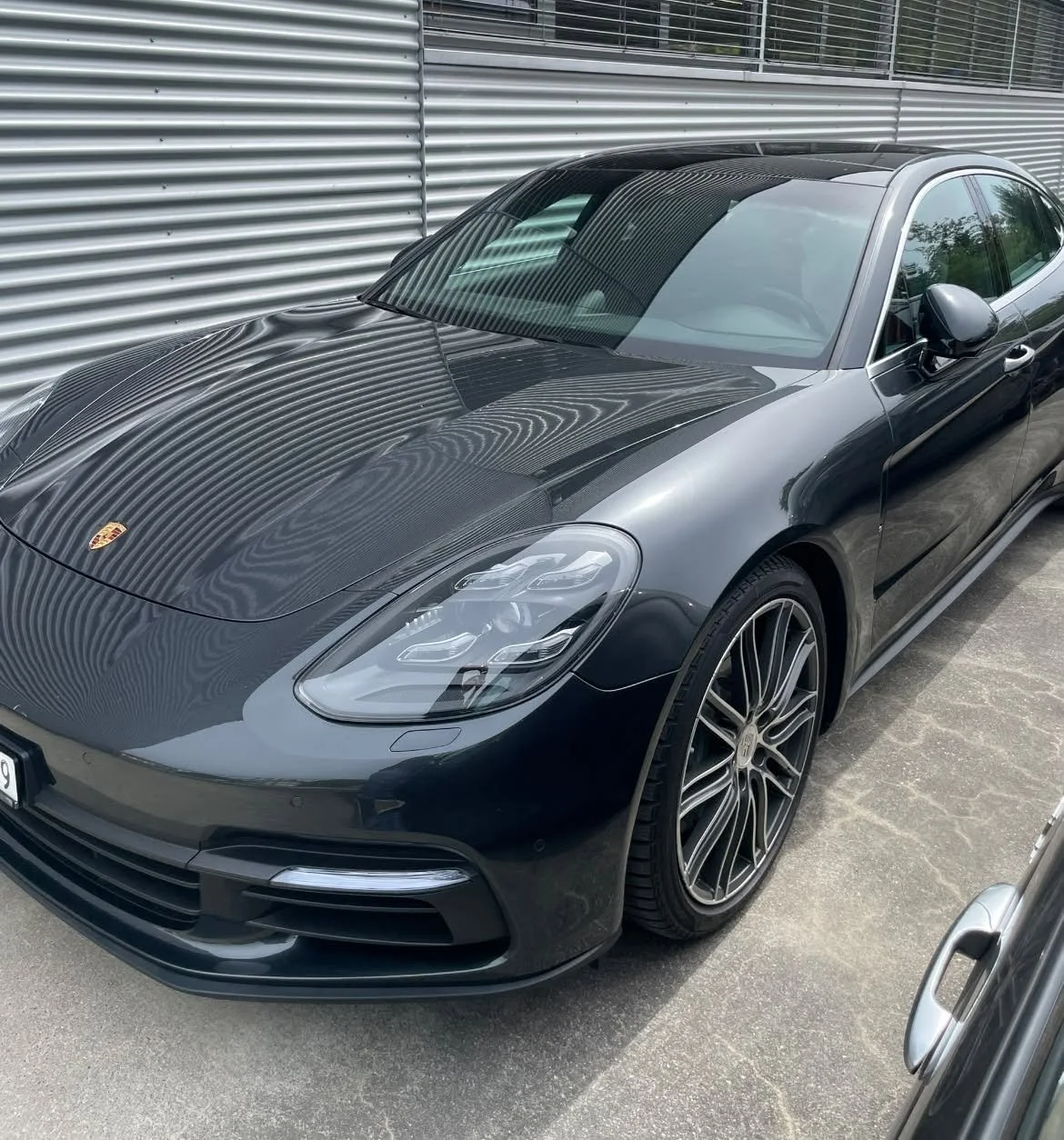 Schwarzer Porsche Sportwagen mit Carbon-Fronthaube und sportlichen Leichtmetallrädern, parkt an einer Metallwand