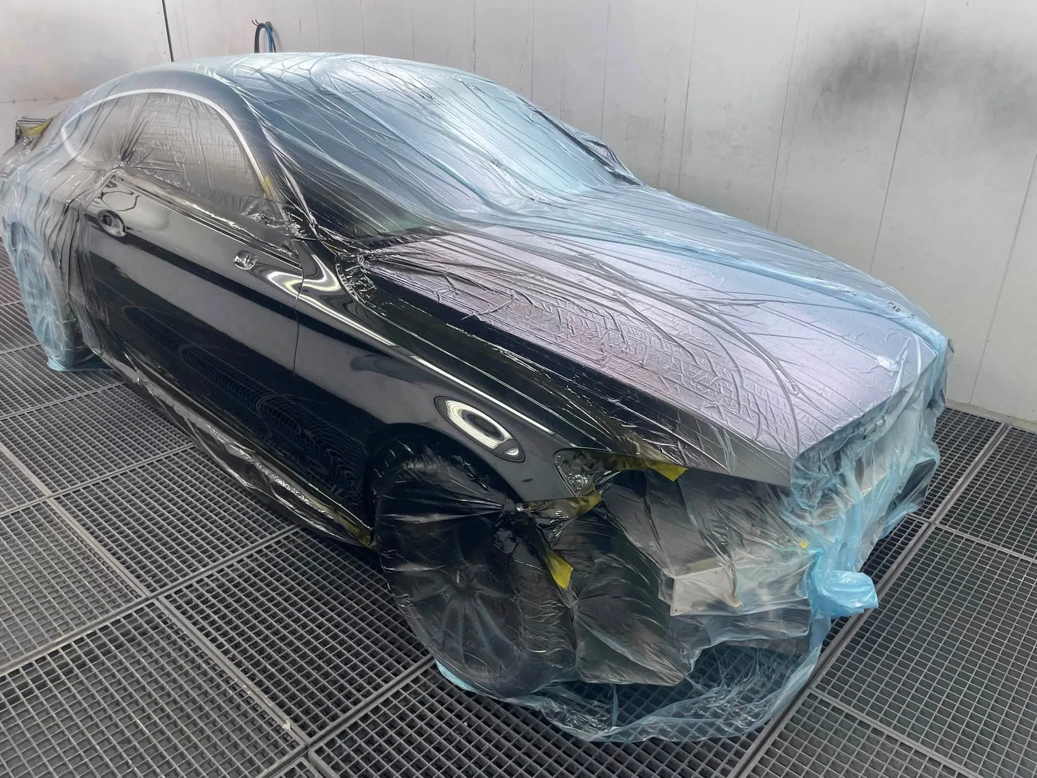 Ein schwarzes Auto wird in einer Lackiererei versiegelt, um es zu schützen, während es lackiert wird.