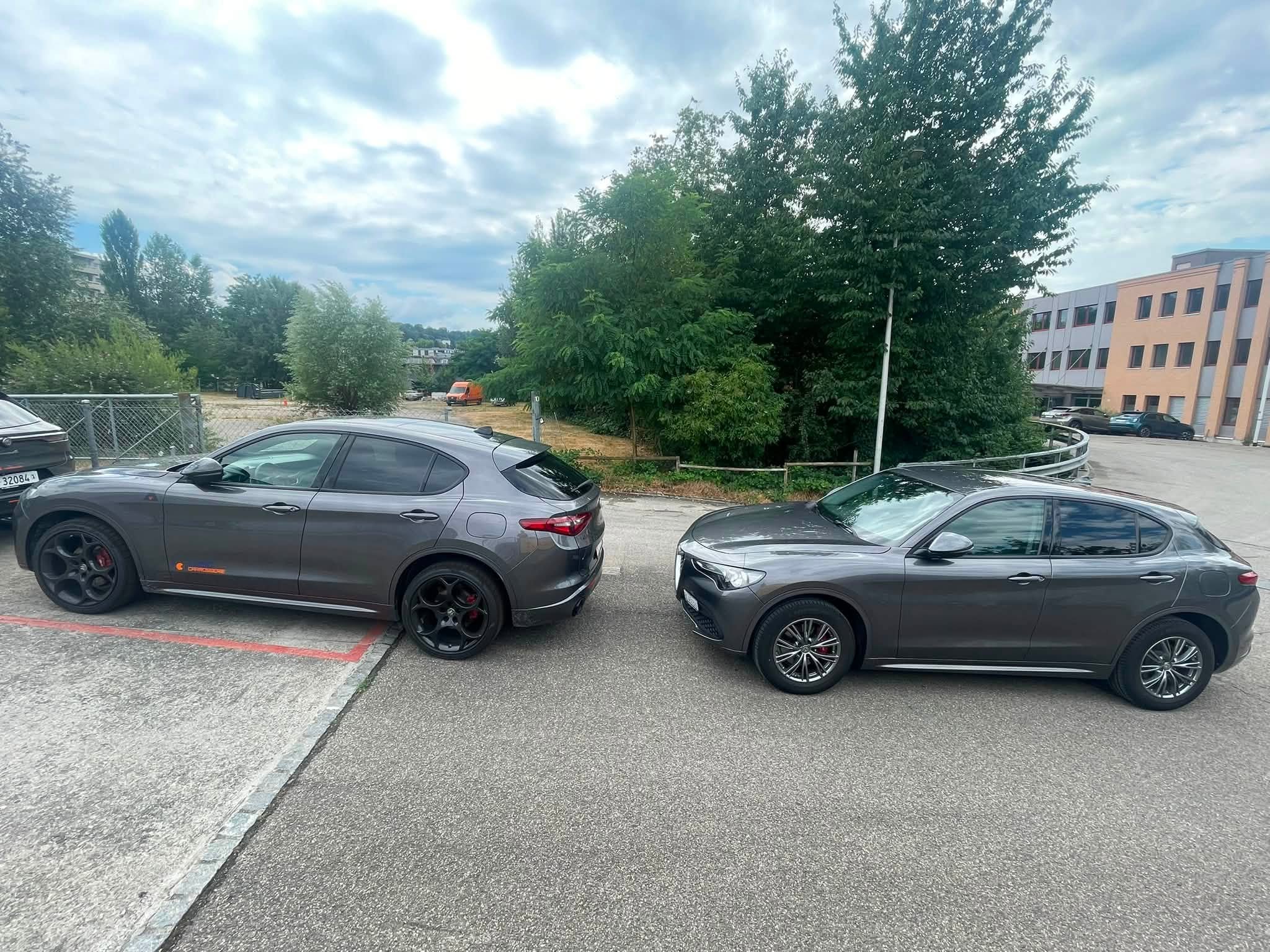 Mehrere parkende Autos vor einem Gebäude mit Bäumen im Hintergrund.