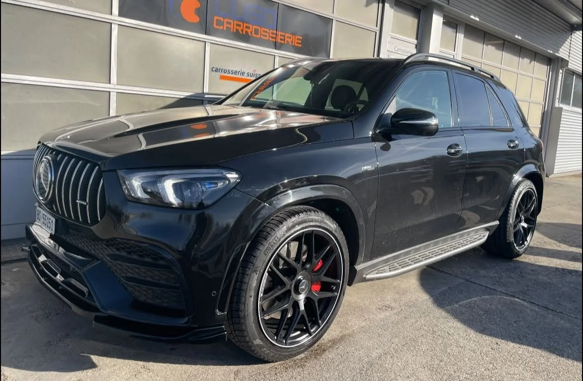 Schwarzer Mercedes-Benz SUV mit sportlichen Felgen, stehen vor einem Gebäude mit Beschilderung 'Carrosserie' auf der Fensterfassade.