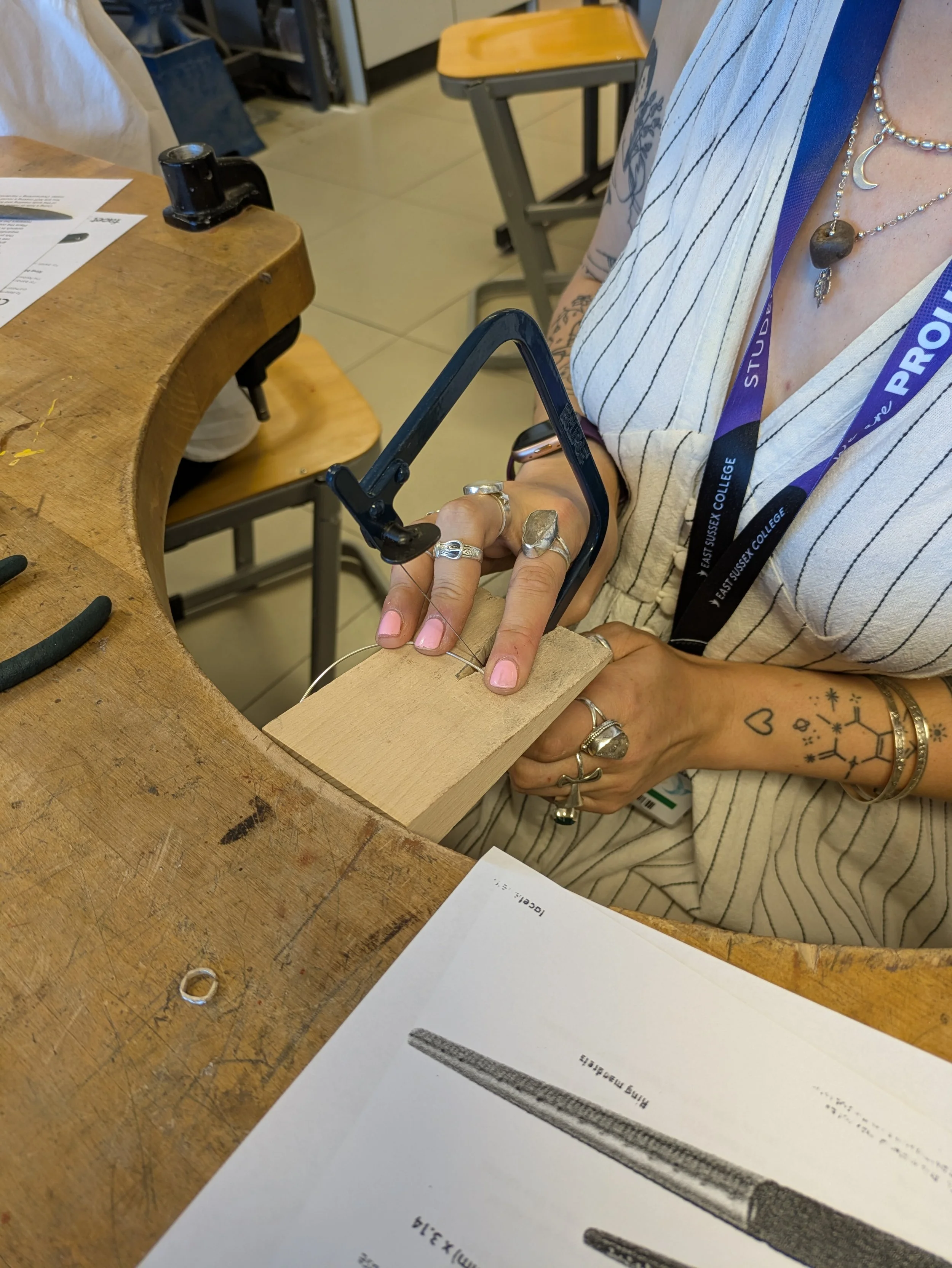 Grace's hands on a workbench, cutting through a silver wire hoop.