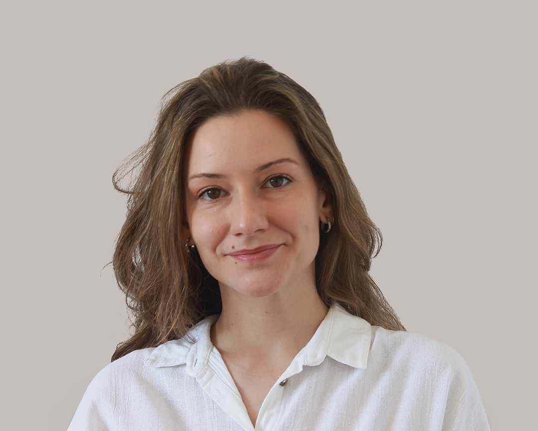 Retrato profesional de Joanna Alba, psicóloga, con cabello castaño y ropa blanca sobre un fondo gris