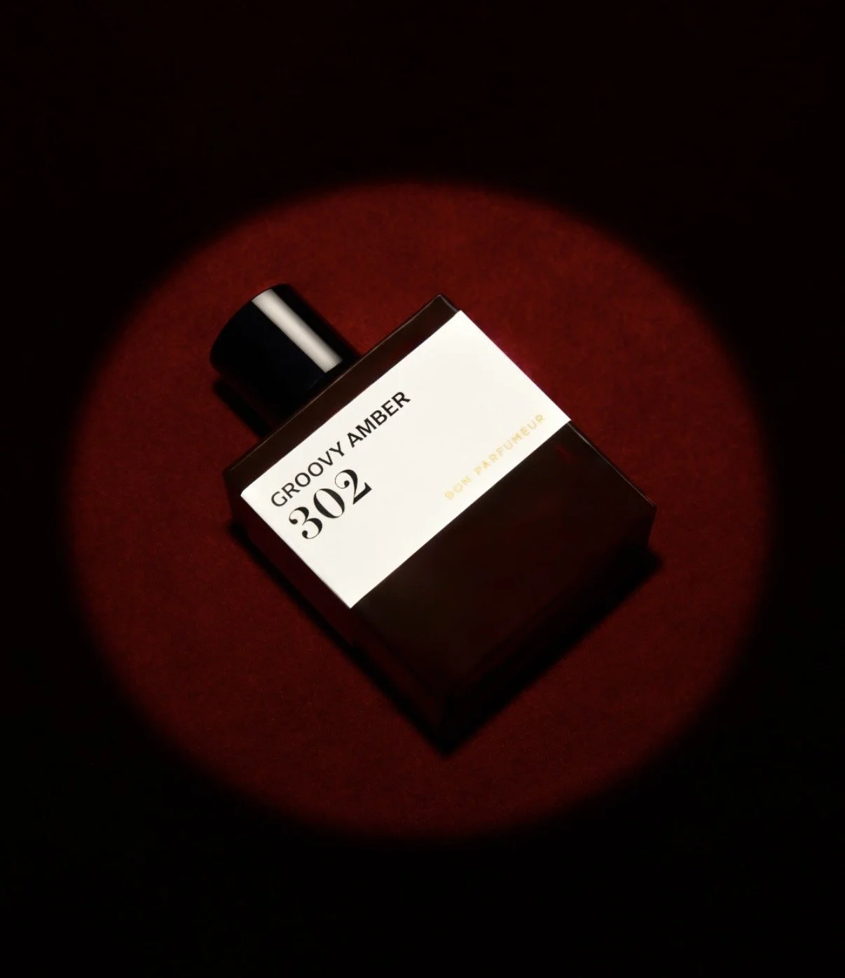 A perfume bottle labeled 'Groovy Amber 302' by Don Perfume on a red surface, illuminated by a focused light, with a dark background.
