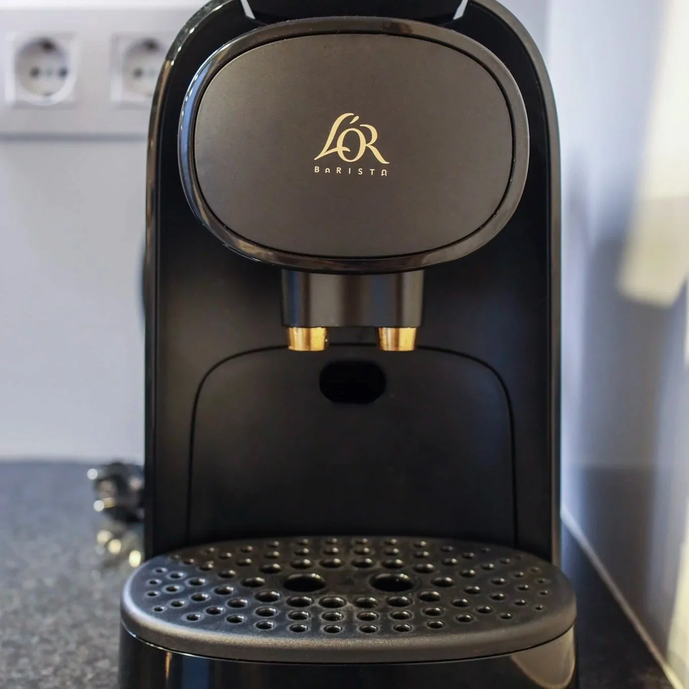 Máquina de café espresso negra con logo de L'OR en la parte superior, en una encimera de cocina.