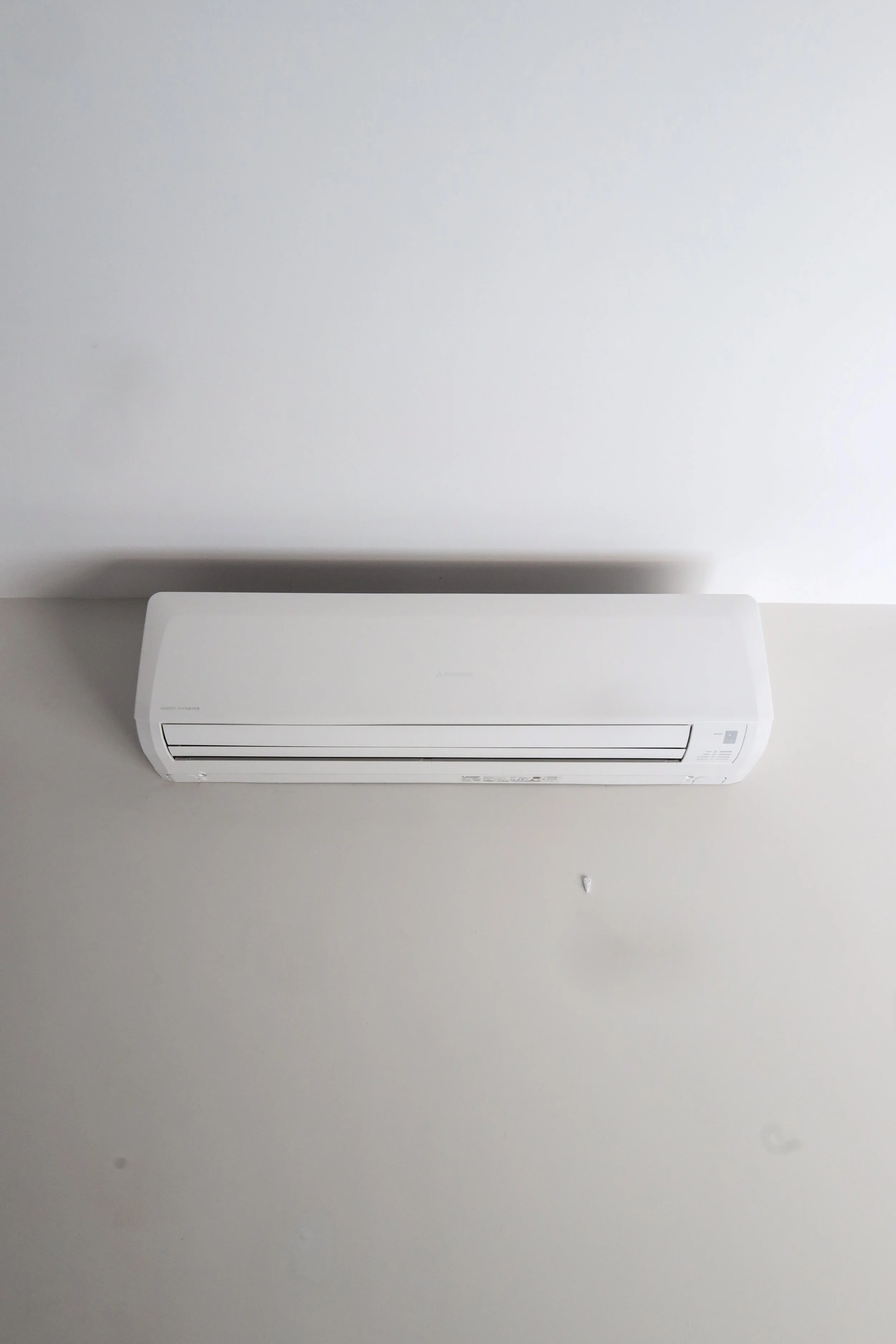 Aire acondicionado blanco instalado en la pared de un cuarto con techo blanco.