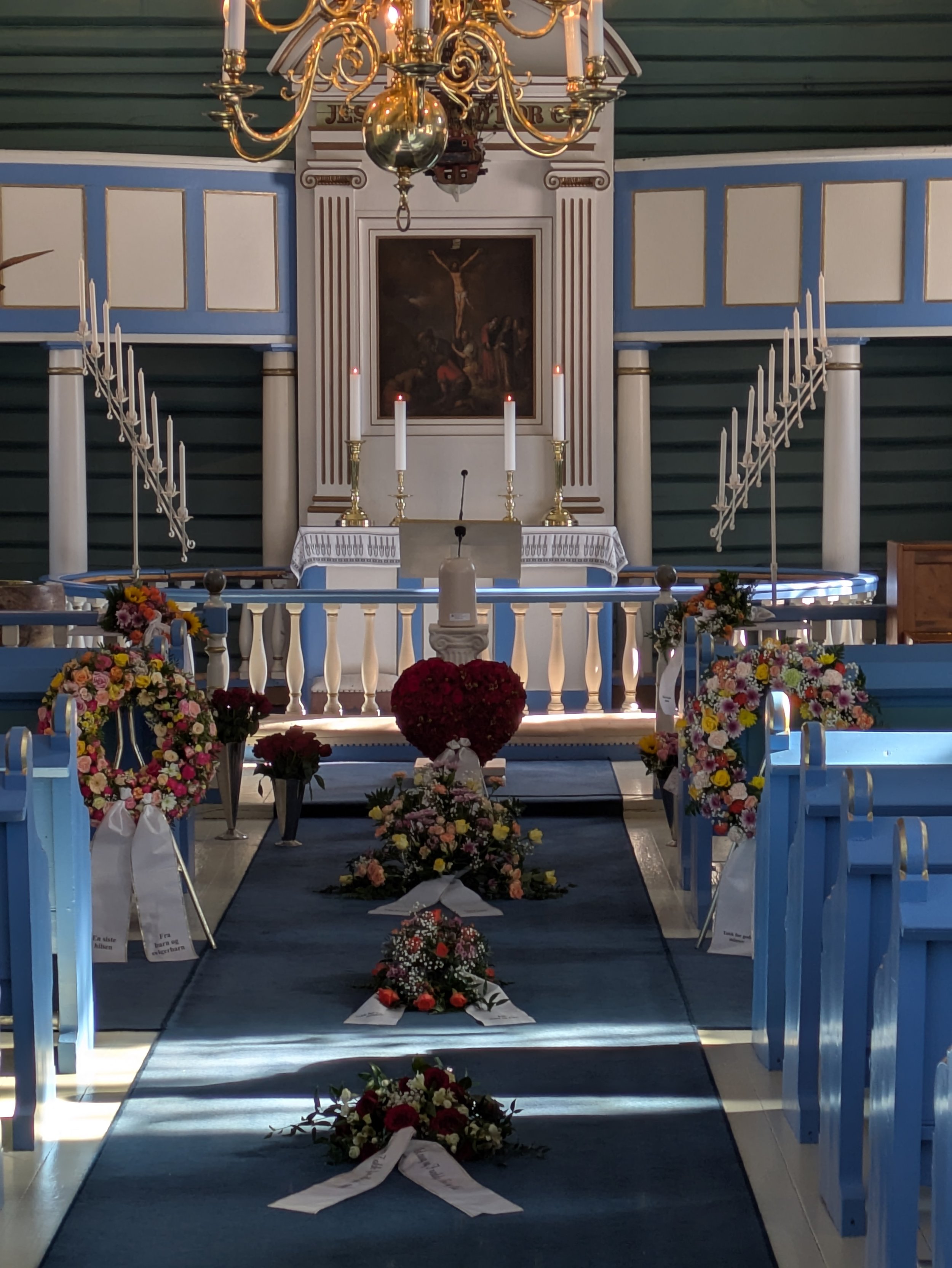 Kirkesal med alter, blomsterdekorationer, kors og fettcandelabre, brukt til en seremoni eller gudstjeneste.
