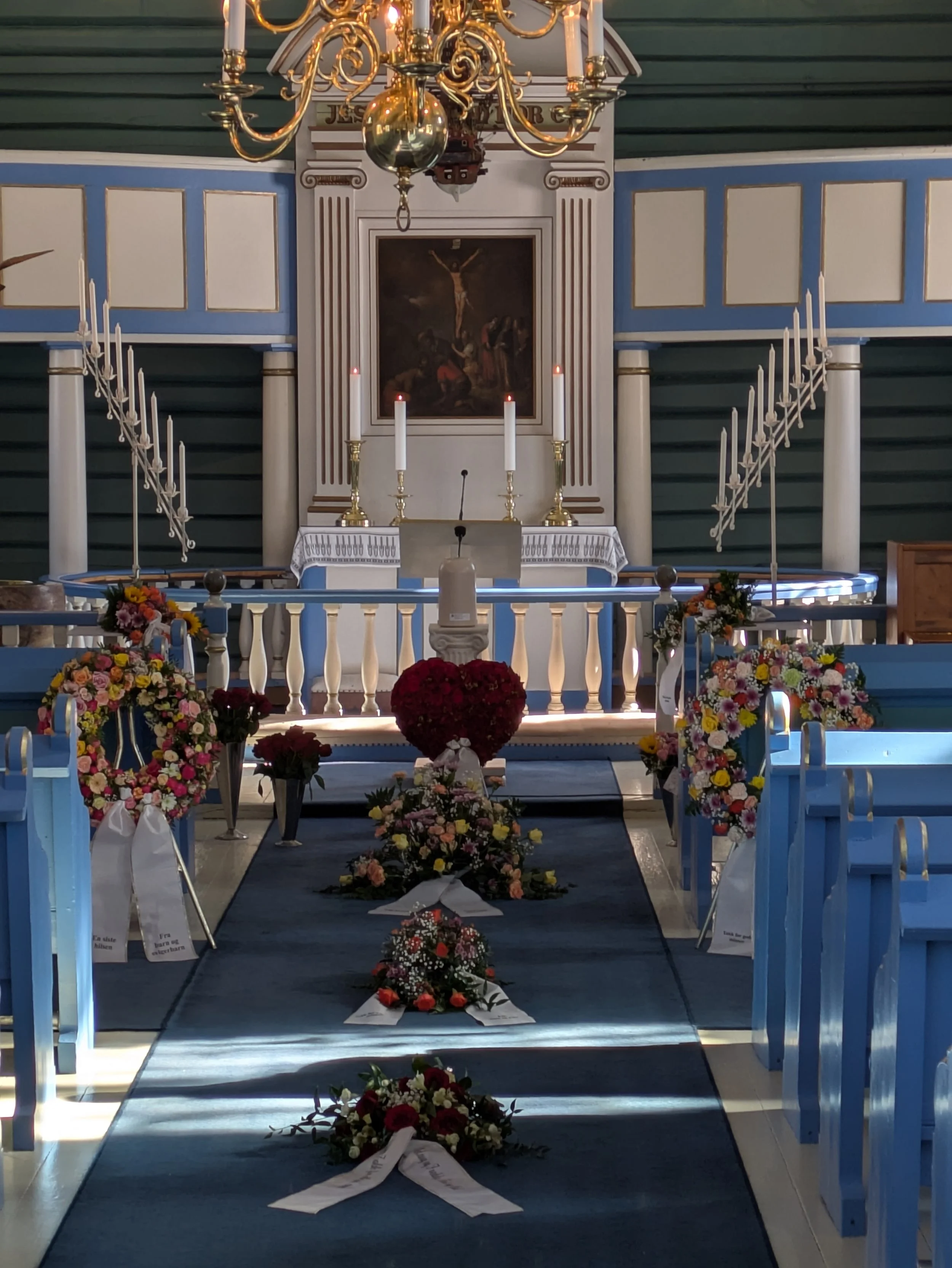 Interiør av en kirke med alter, blomsterarrangementer, stearinlys, og et bilde av Jesus på korset bak alteret.
