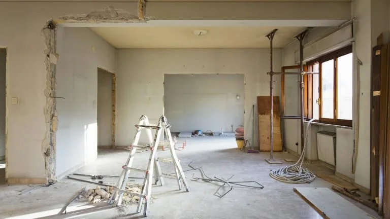 Undergoing renovation, an unfinished room with construction tools and scaffolding, exposed walls, and a large window.