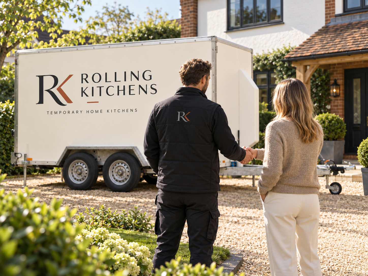 A man and woman shaking hands in front of a mobile kitchen trailer with the logo 'Rolling Kitchens' in a residential neighborhood.