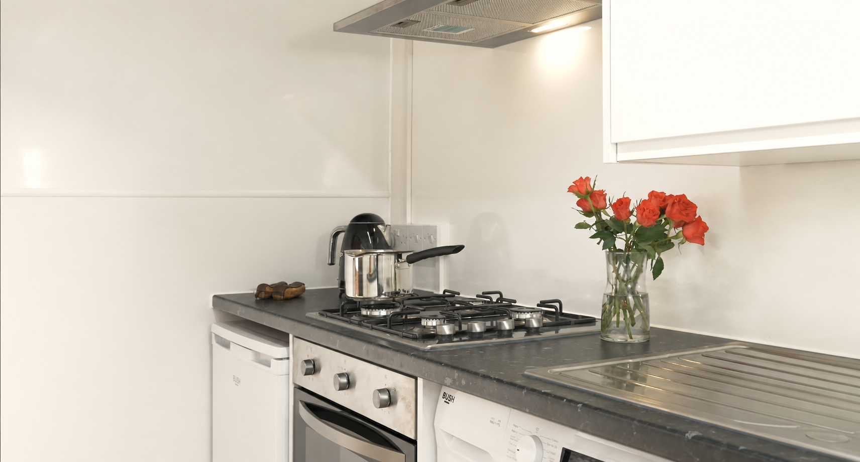 Kitchen countertop with a kettle, a saucepan on a stove, a fruit knife, a vase of red roses, and an oven.