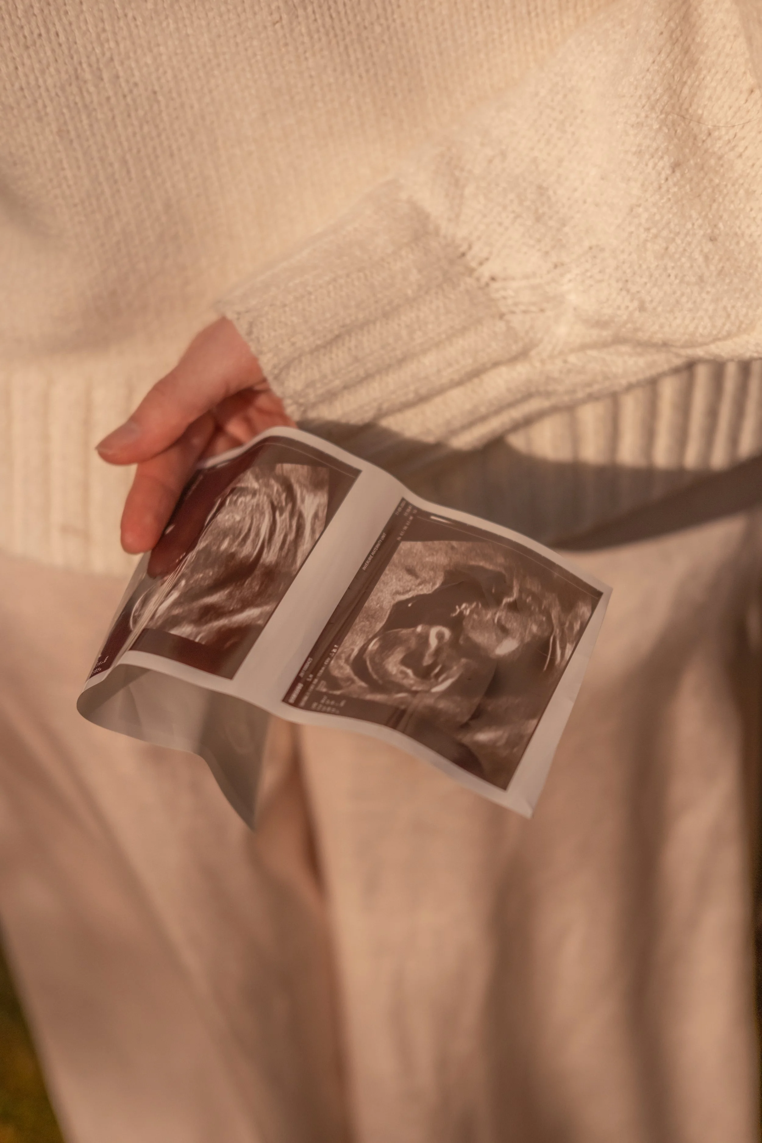 A person wearing a beige sweater holding an ultrasound image.