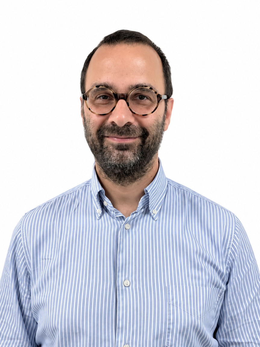 Man with dark hair and beard wearing glasses and a blue striped shirt, standing against a white background.