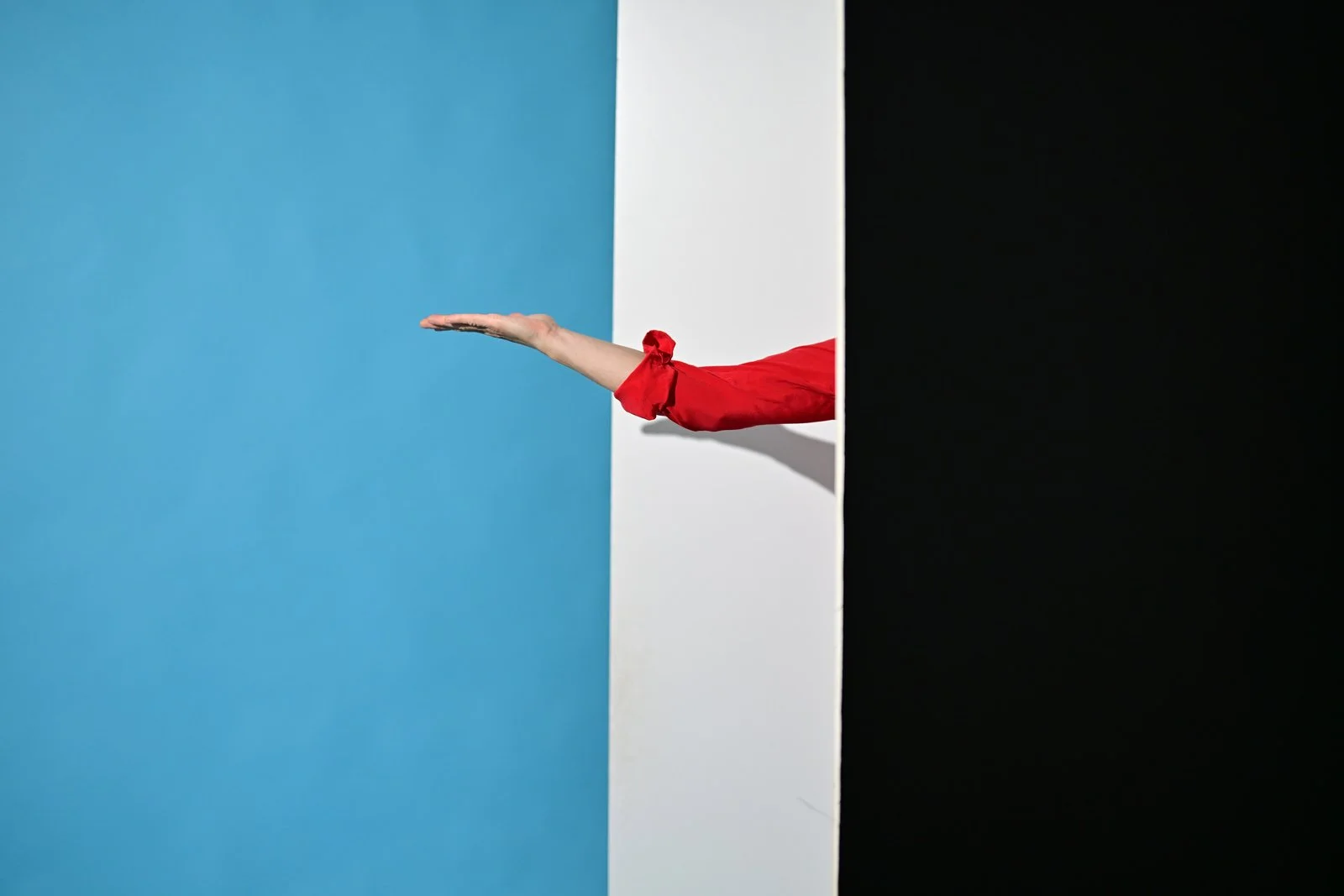 Ein Arm in rotem Kleid, der aus einem schwarzen, weißen und blauen Hintergrund herausragt, mit der Hand, die einen ausgestreckten, flachen Hand zeigt.
