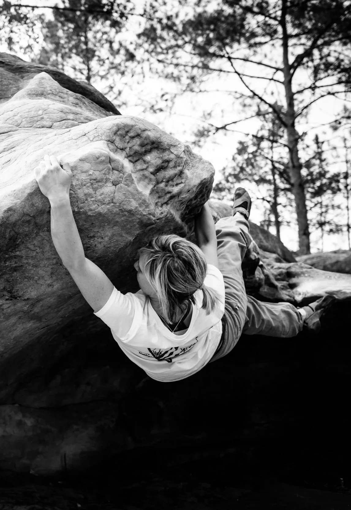 Frau beim Boulder in Fontainebleau an einem Felsen. Schwarz-Weiß-Foto in einer natürlichen, bewaldeten Umgebung.