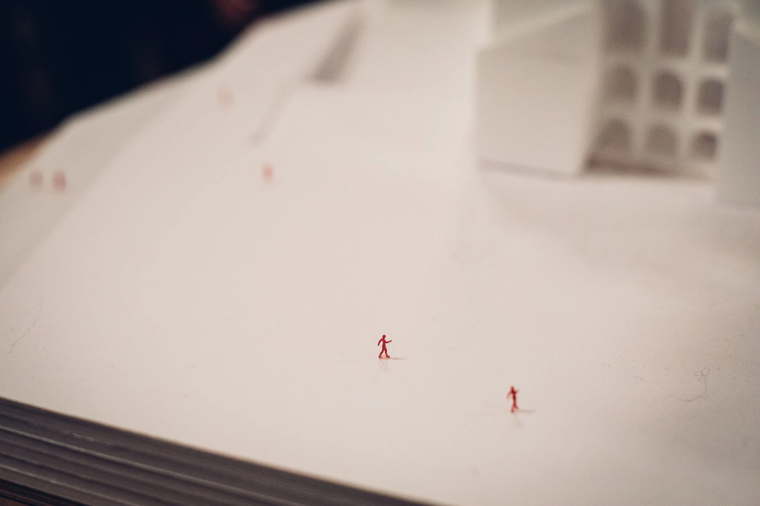Ein rotes Miniatur-Mensch-Modell auf einer Seite eines Buches, darunter sind zwei weitere Miniatur-Menschen. Im Hintergrund ist eine Tastatur zu sehen.