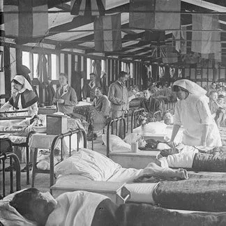 A WW1 hospital ward showing rows of beds with patients in an Nurses tending to them.