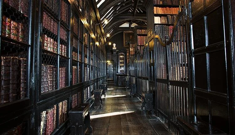 Chetham Library showing dark wood and ornate books lining the shelves of a coridor.