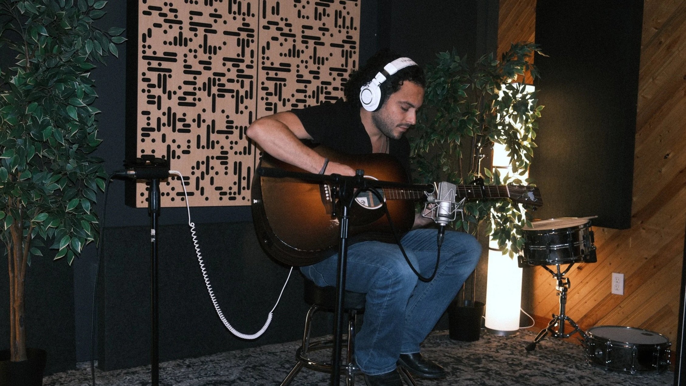 Un artiste assis dans la salle d'enregistrement du Studio Agora en train d'enregistrer sa voix et sa guitare.