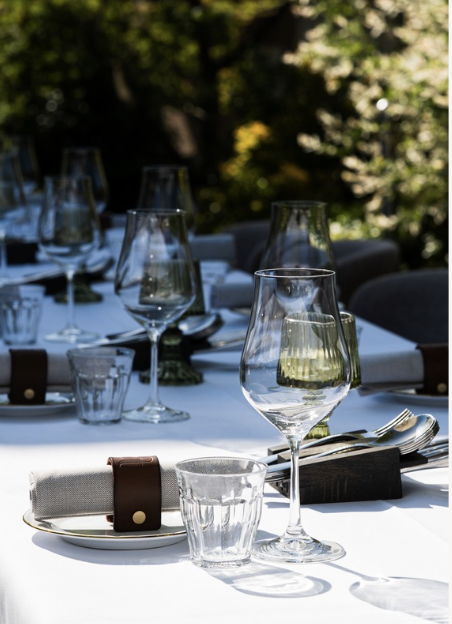 Een tafel gedekt voor een maaltijd, met wijnglazen, waterglazen, borden en bestek in een tuin of buitenomgeving.