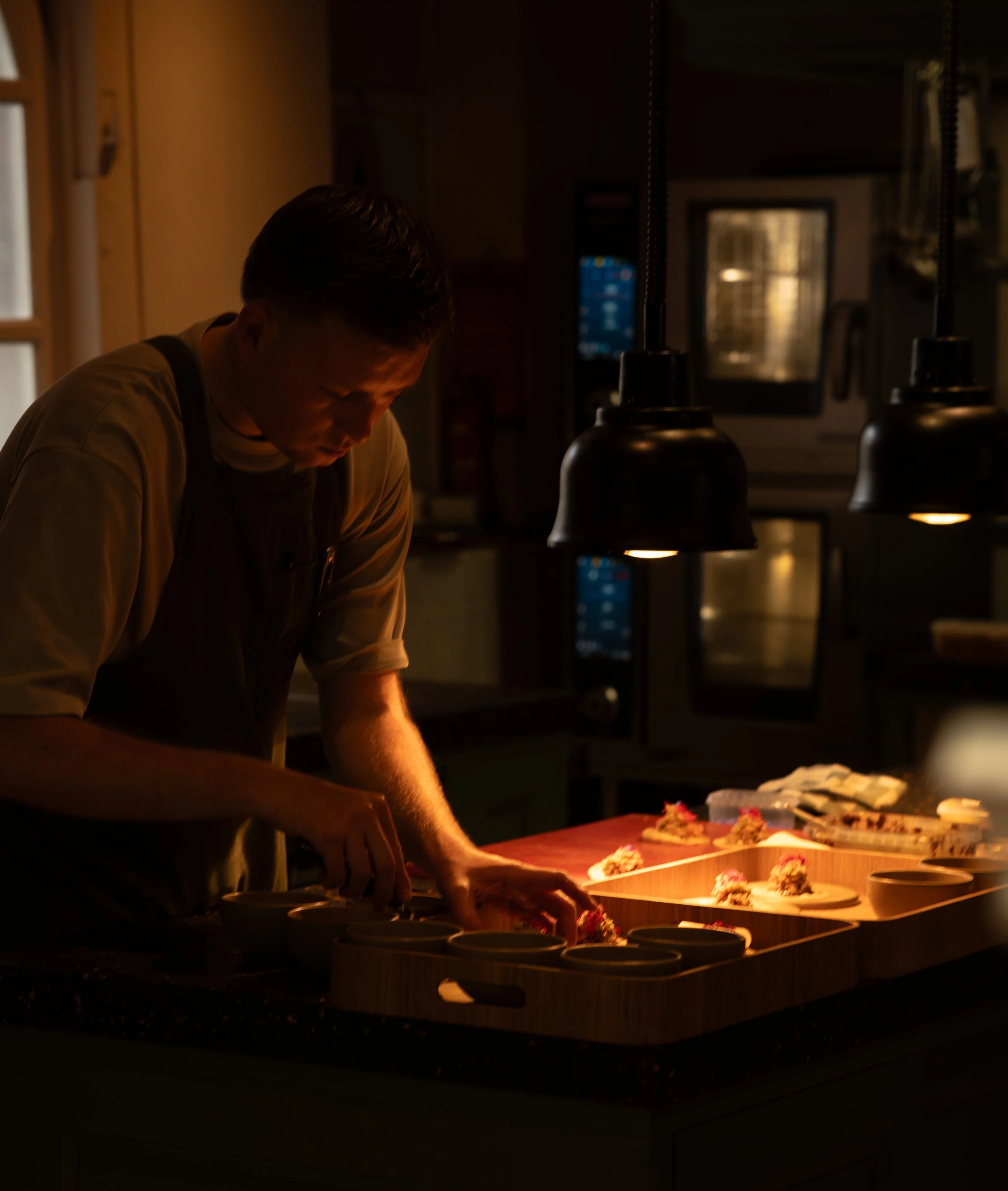 Een persoon die zich bezighoudt met het serveren van eten in een keuken met warme verlichting.