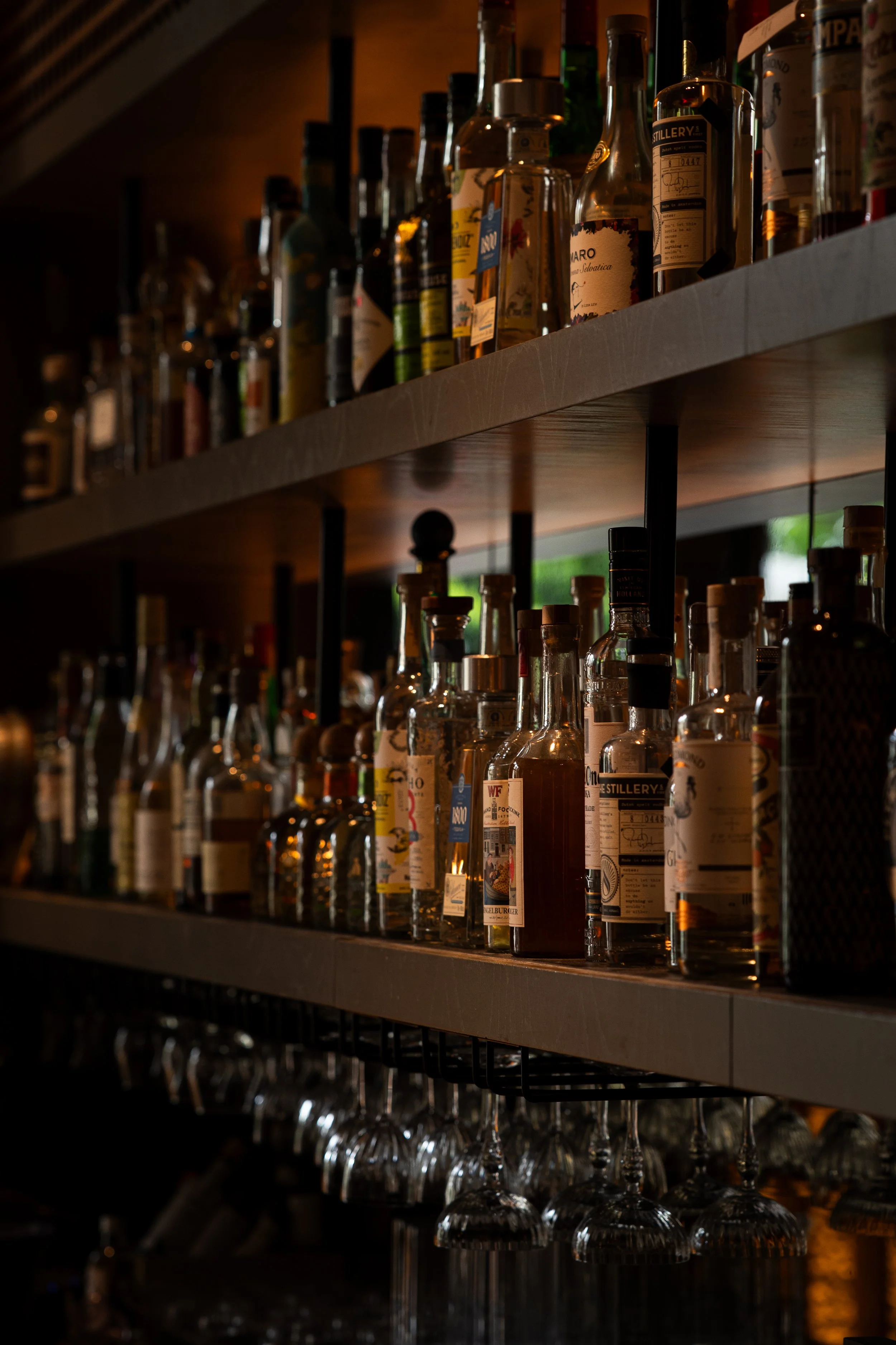 Een boekenkast met diverse flessen alcohol en wijn, met onderaan wijnglazen.