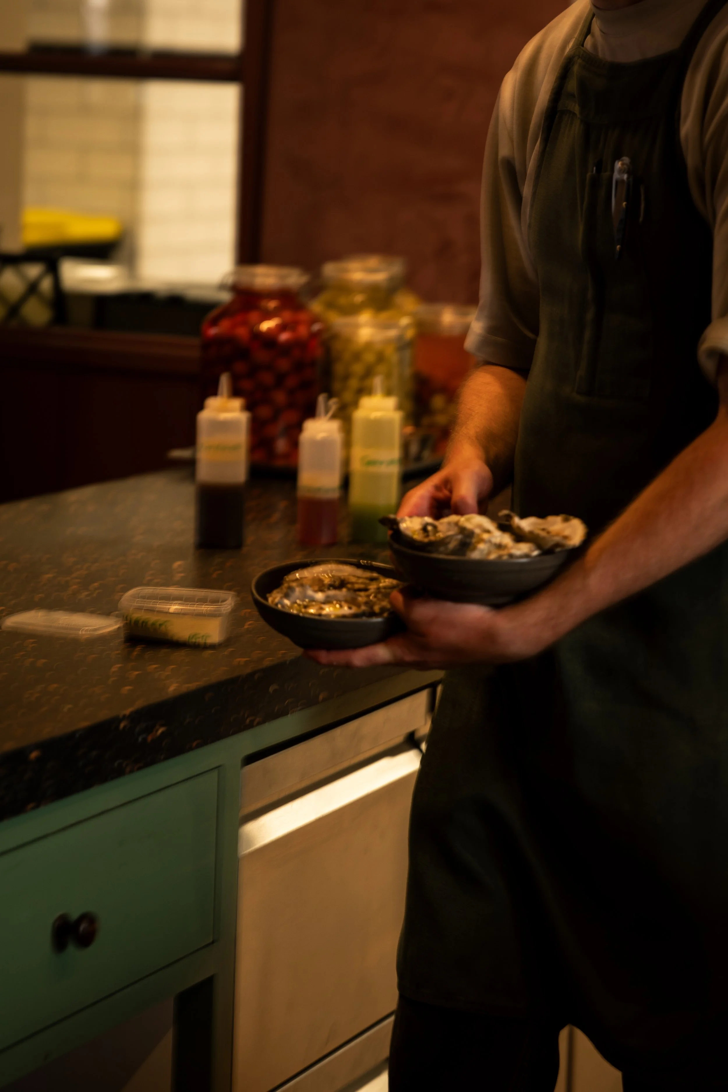 Man serveert zeevruchten in een restaurant met potten augurken op de achtergrond.