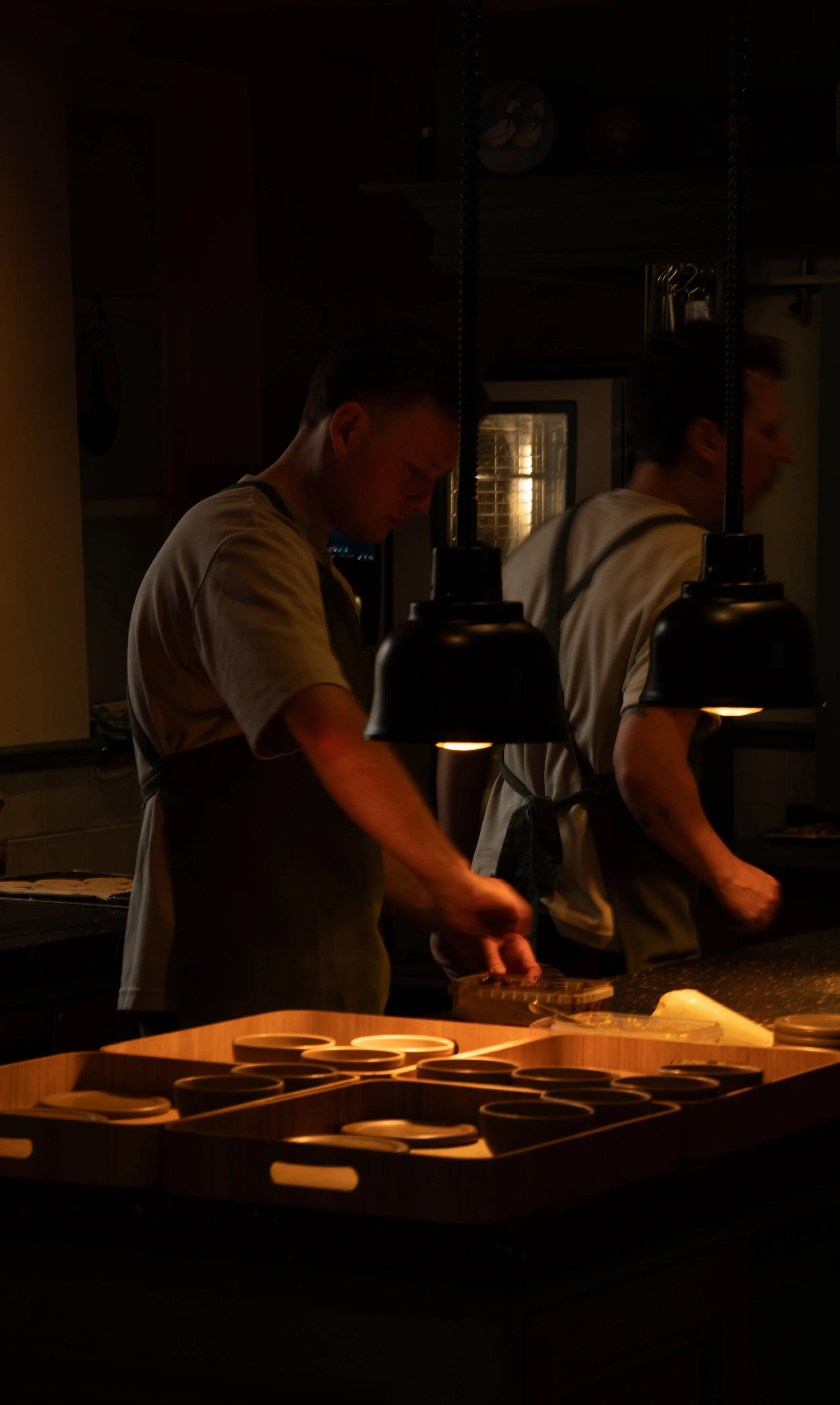 Twee chefs bereiden gerechten in een professionele keuken, verlicht door warme lampen, met een overzicht van kleine ronde borden op de voorgrond.