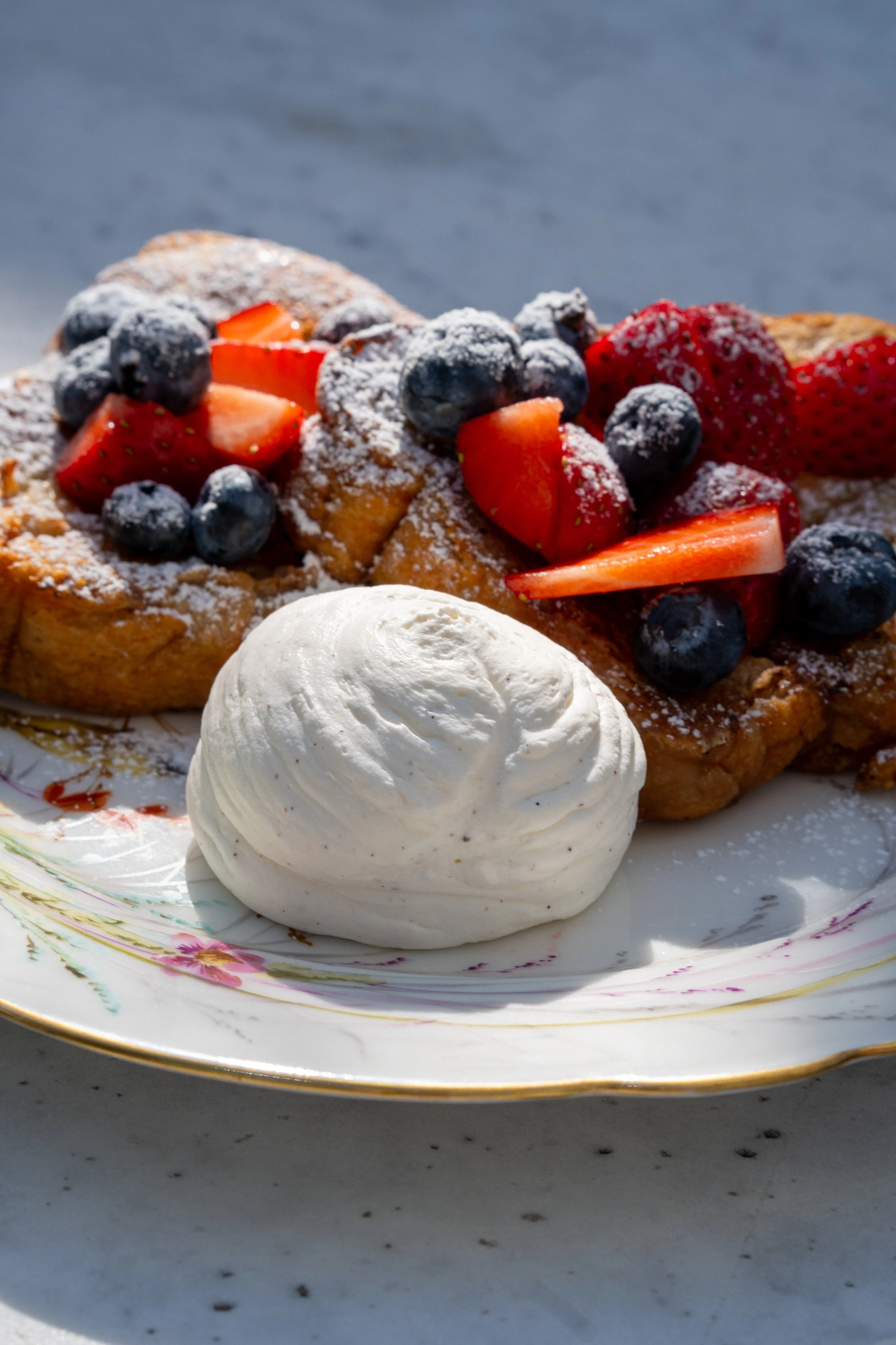 Een bord met Franse stijl, gevuld met wafels, vers fruit zoals aardbeien en blauwe bessen, poedersuiker, en een klodder slagroom.