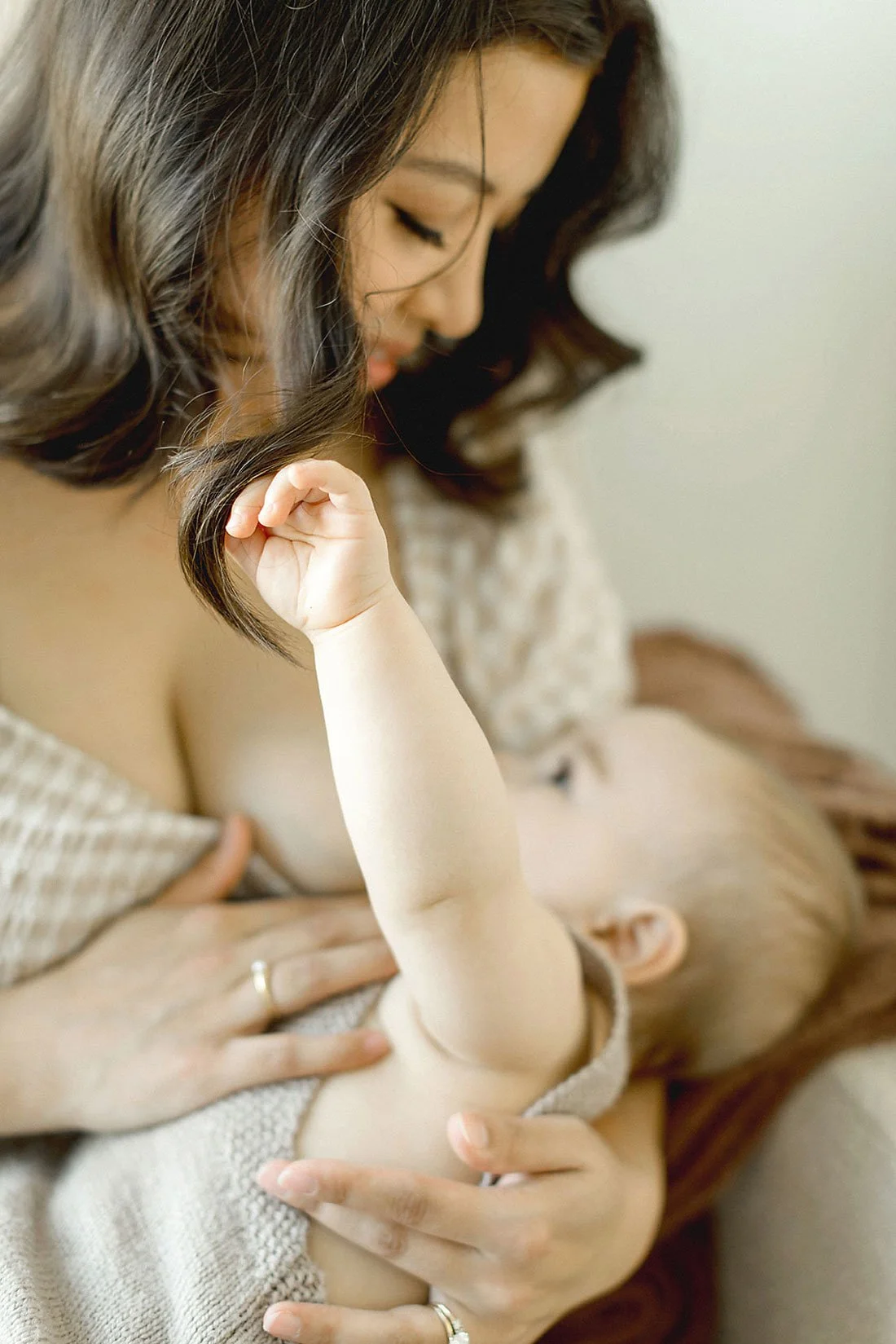 A woman holding a baby, gently pressing her chest while the baby touches her face and lifts its arm.
