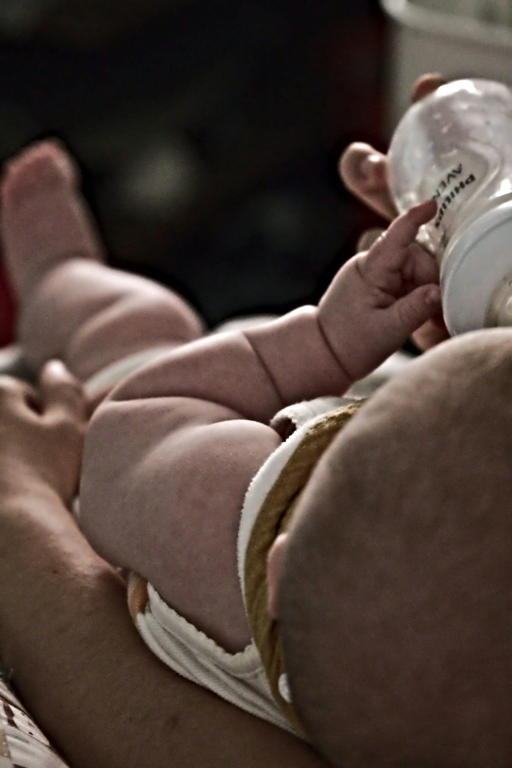 Close-up of a baby's hand holding a small baby bottle.