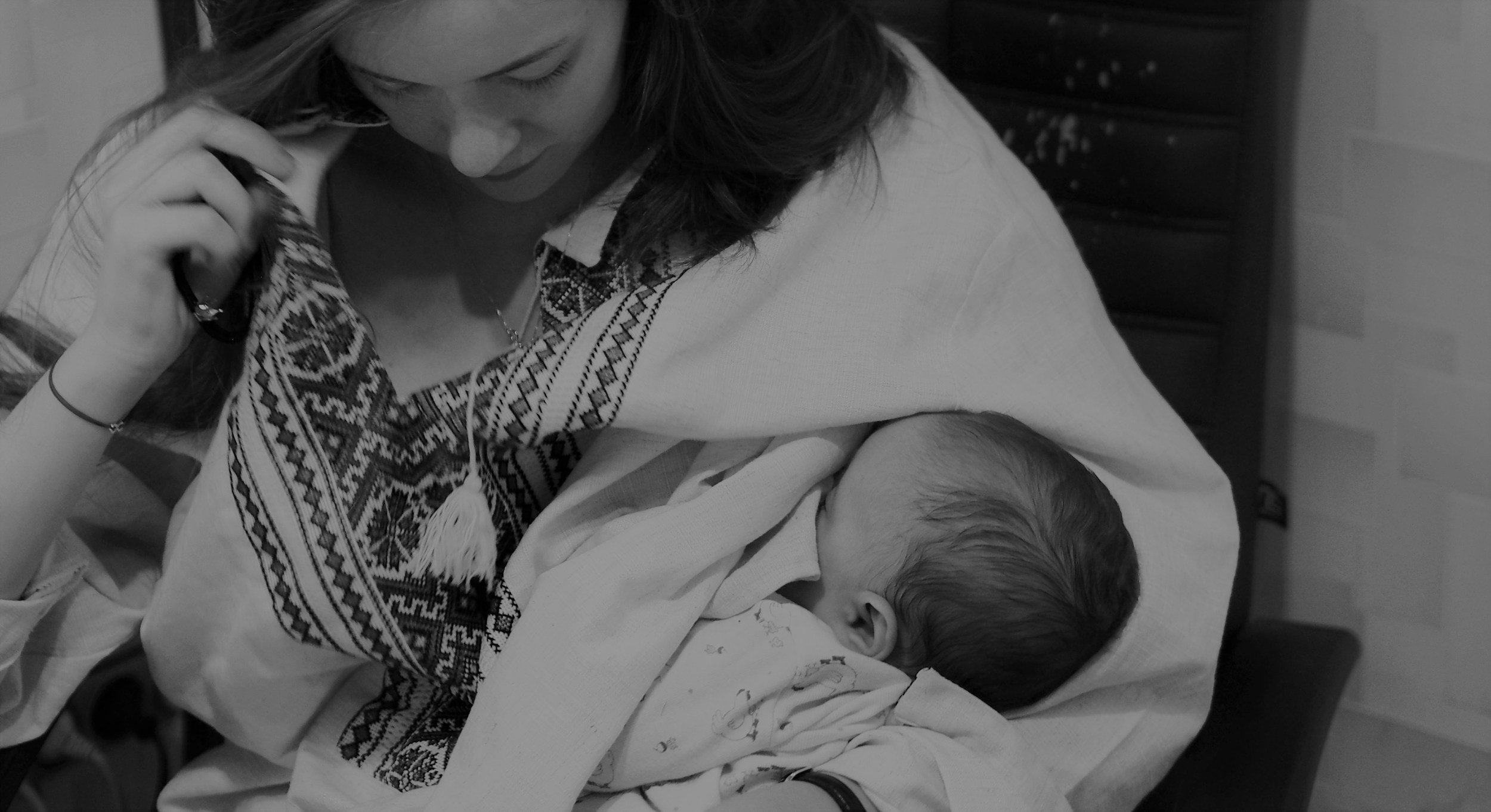 A woman with long dark hair talking on a cell phone while leaning over and holding a young child with short hair who is resting on her lap.