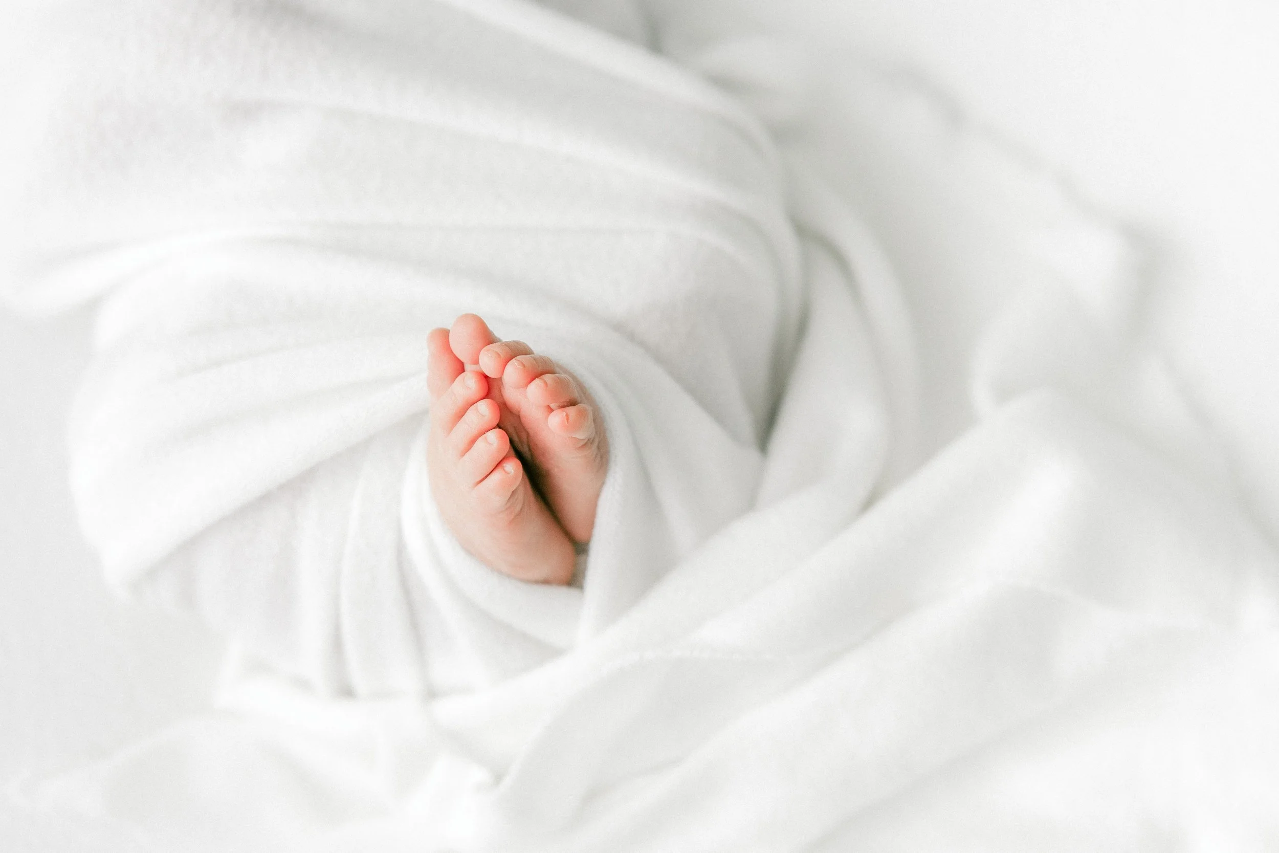 Close-up of tiny newborn baby's feet against white fabric background.