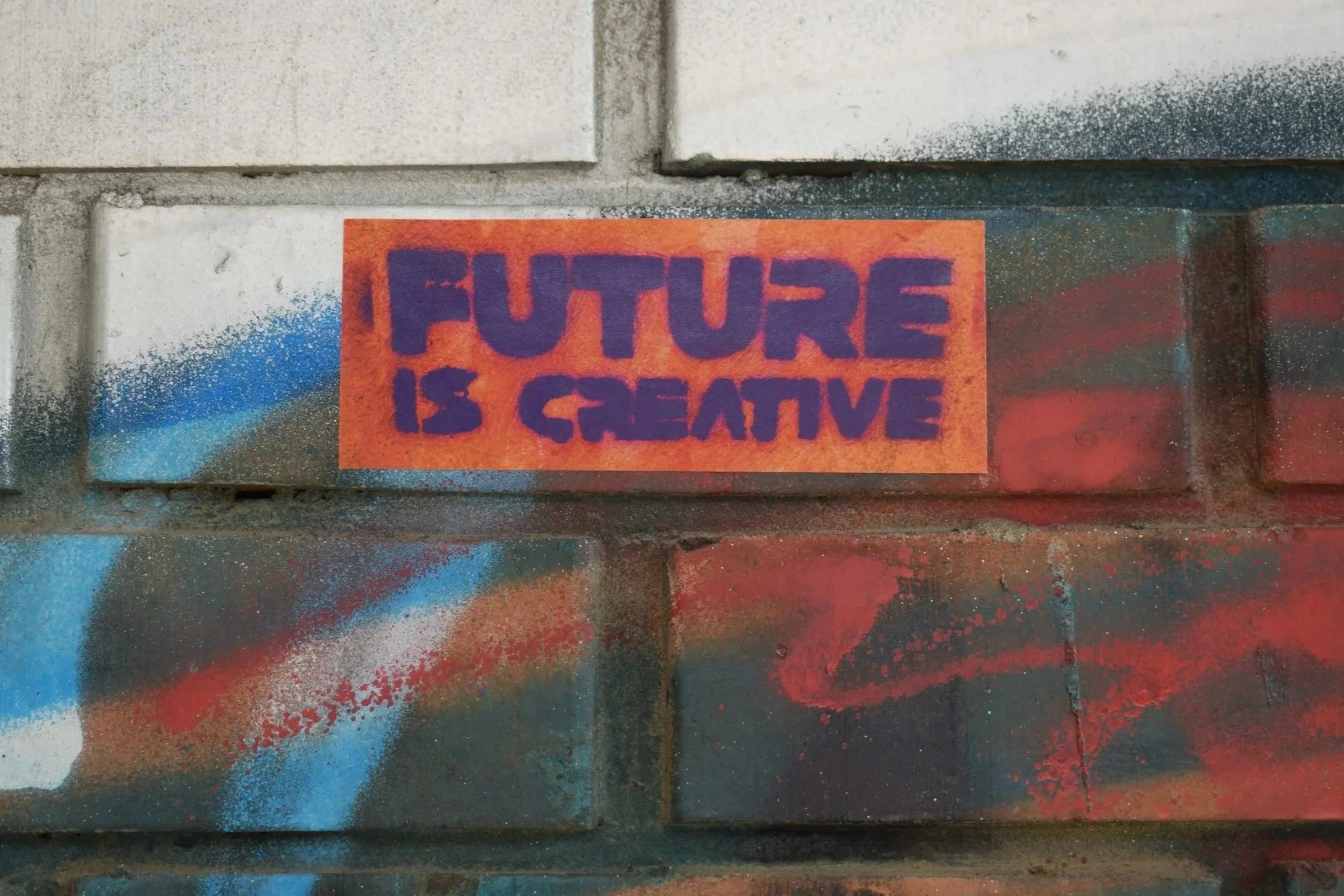 Graffiti-covered brick wall with an orange sticker that reads 'FURE IS CREATIVE' in purple letters.