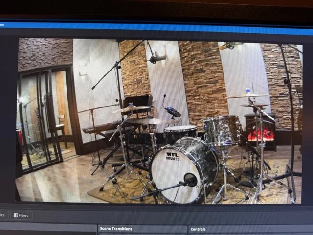 Recording studio with a drum set positioned in front of soundproof walls, microphone stands, and audio equipment.