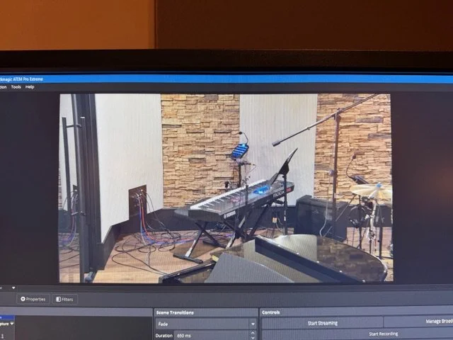 Recording studio or music practice space with keyboard, drums, and microphones set up in a room with brick and white walls.