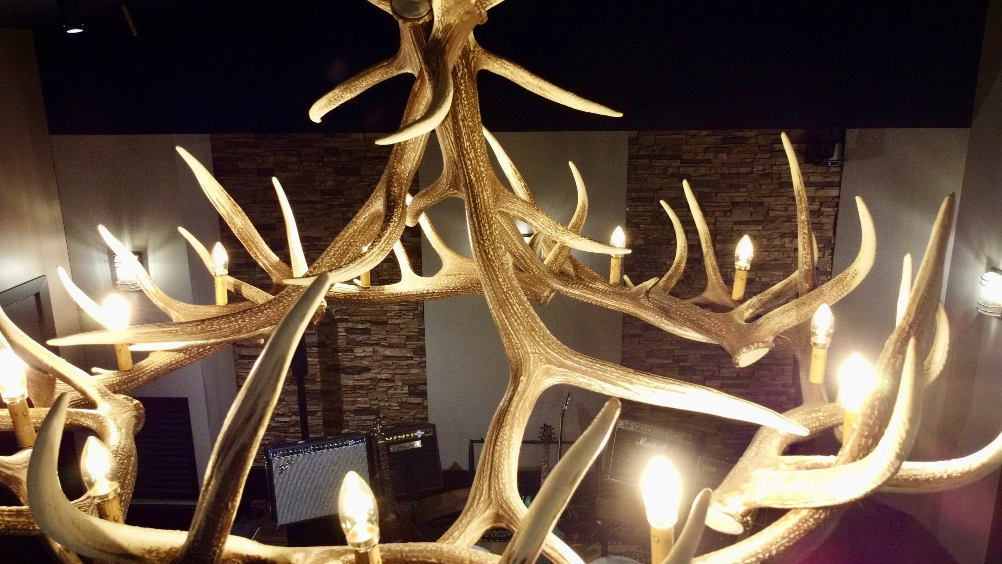 Chandelier made of antlers with light bulbs, mounted on the ceiling of a room with stone wall decor.
