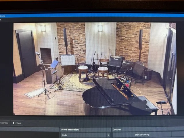 Recording studio with a grand piano, microphones, music stands, and chairs in front of a stone accent wall.